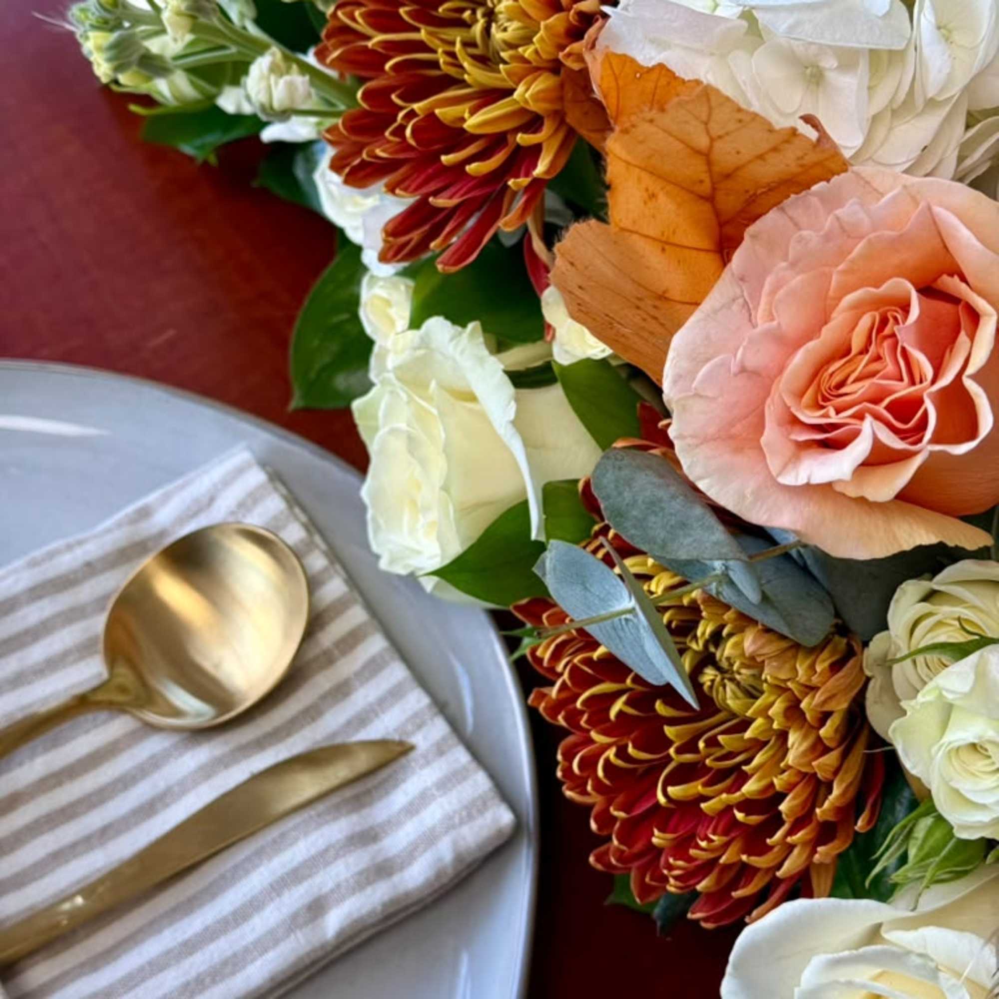 Bouquet of white and peach flowers with orange chrysanthemums beside a place setting