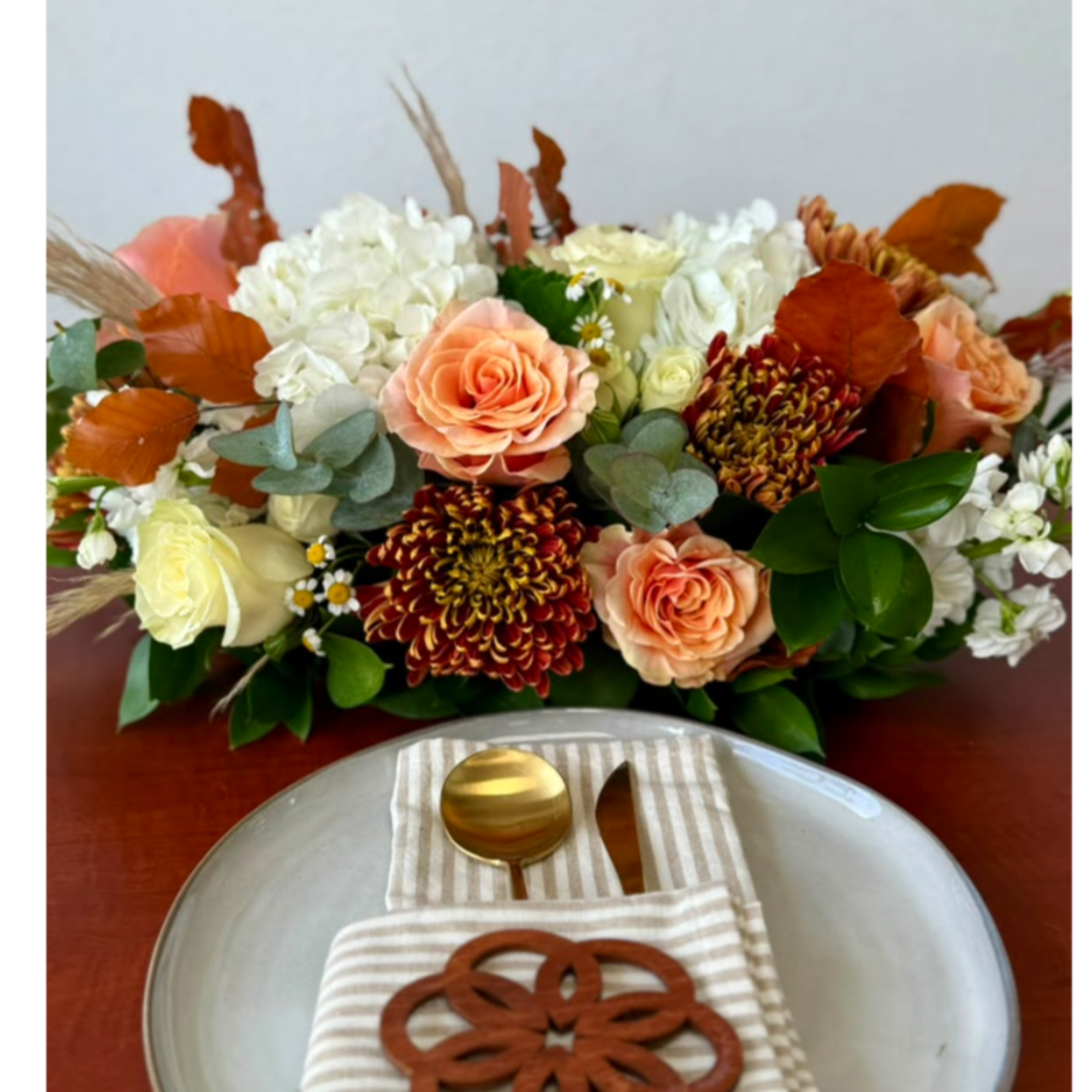 Peach and white floral arrangement with autumn leaves on a table setting