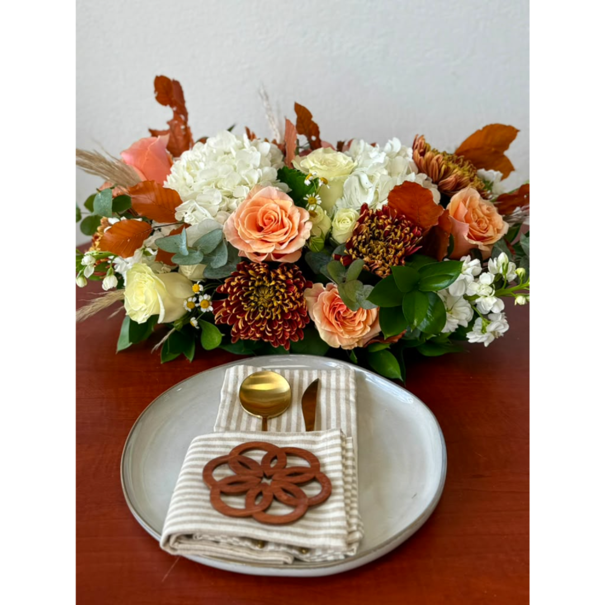 Low floral centerpiece with peach roses, white hydrangeas, and autumn leaves on a table