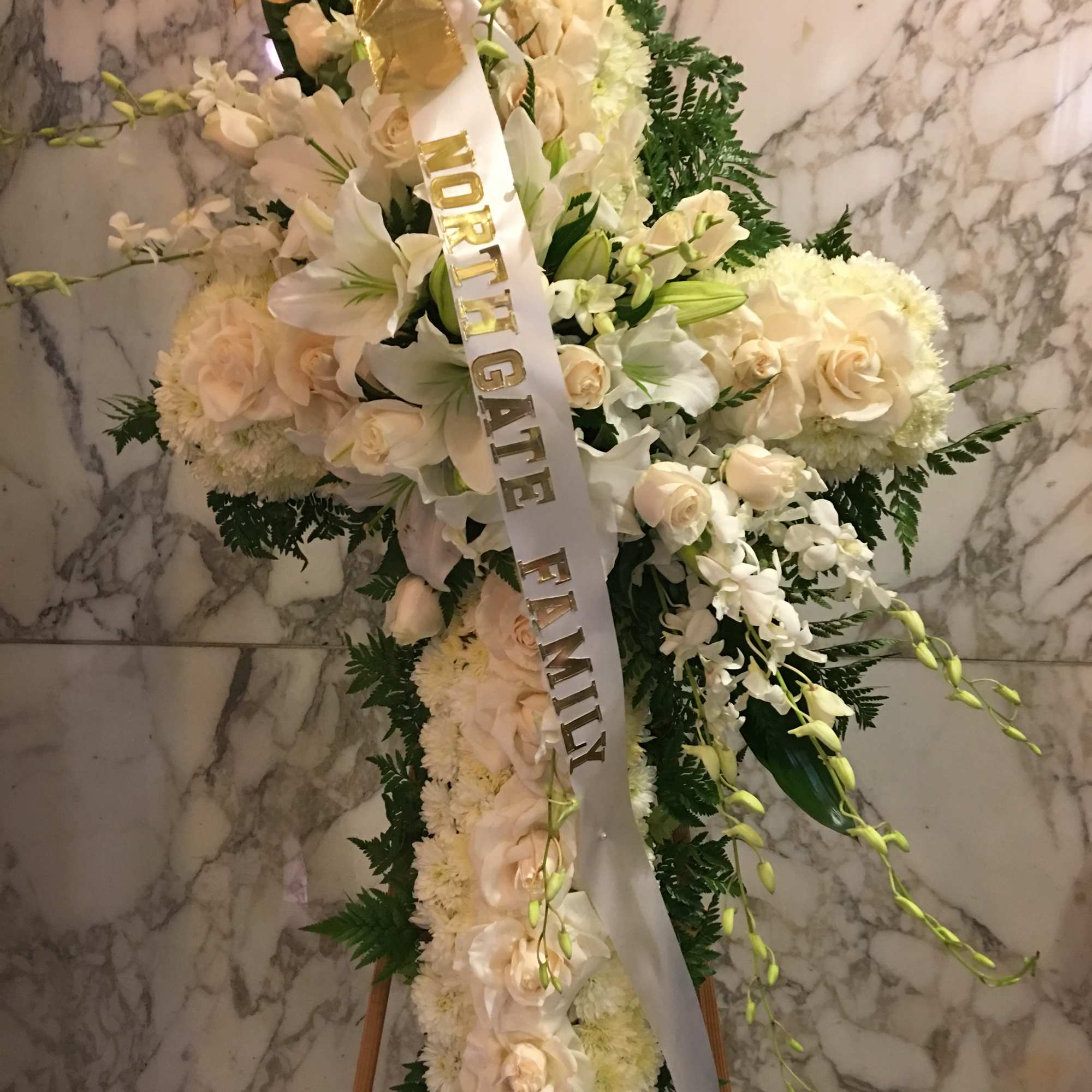 White funeral spray with roses and lilies, accented by a memorial ribbon.