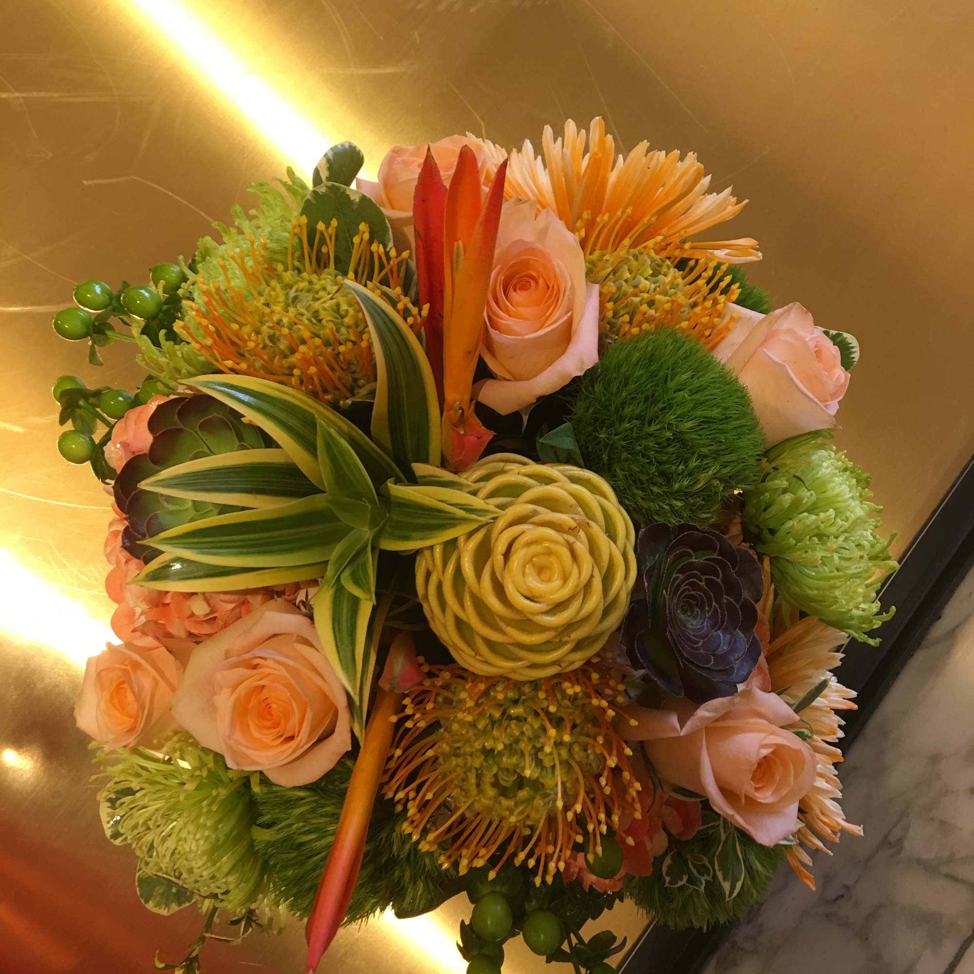 Round bouquet of peach roses and orange tropical blooms with green accents