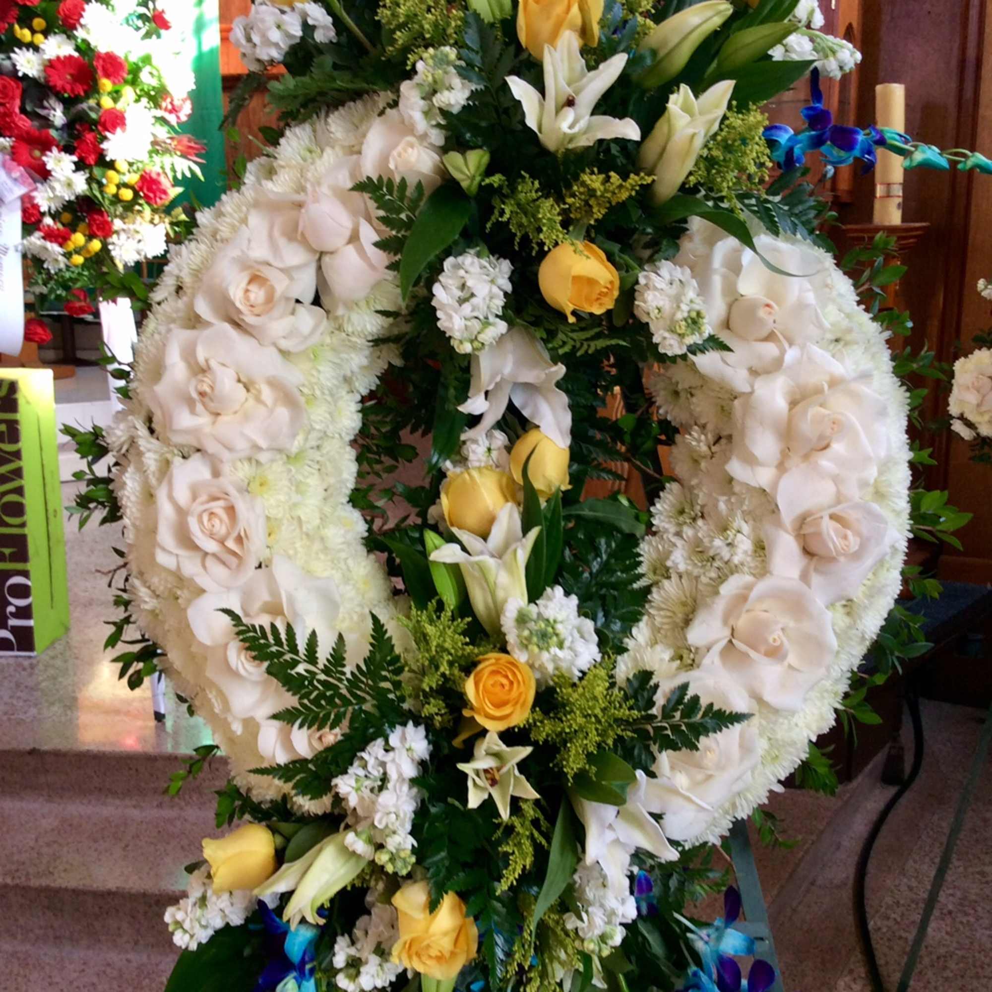 Large floral wreath with white roses, lilies, and yellow accents