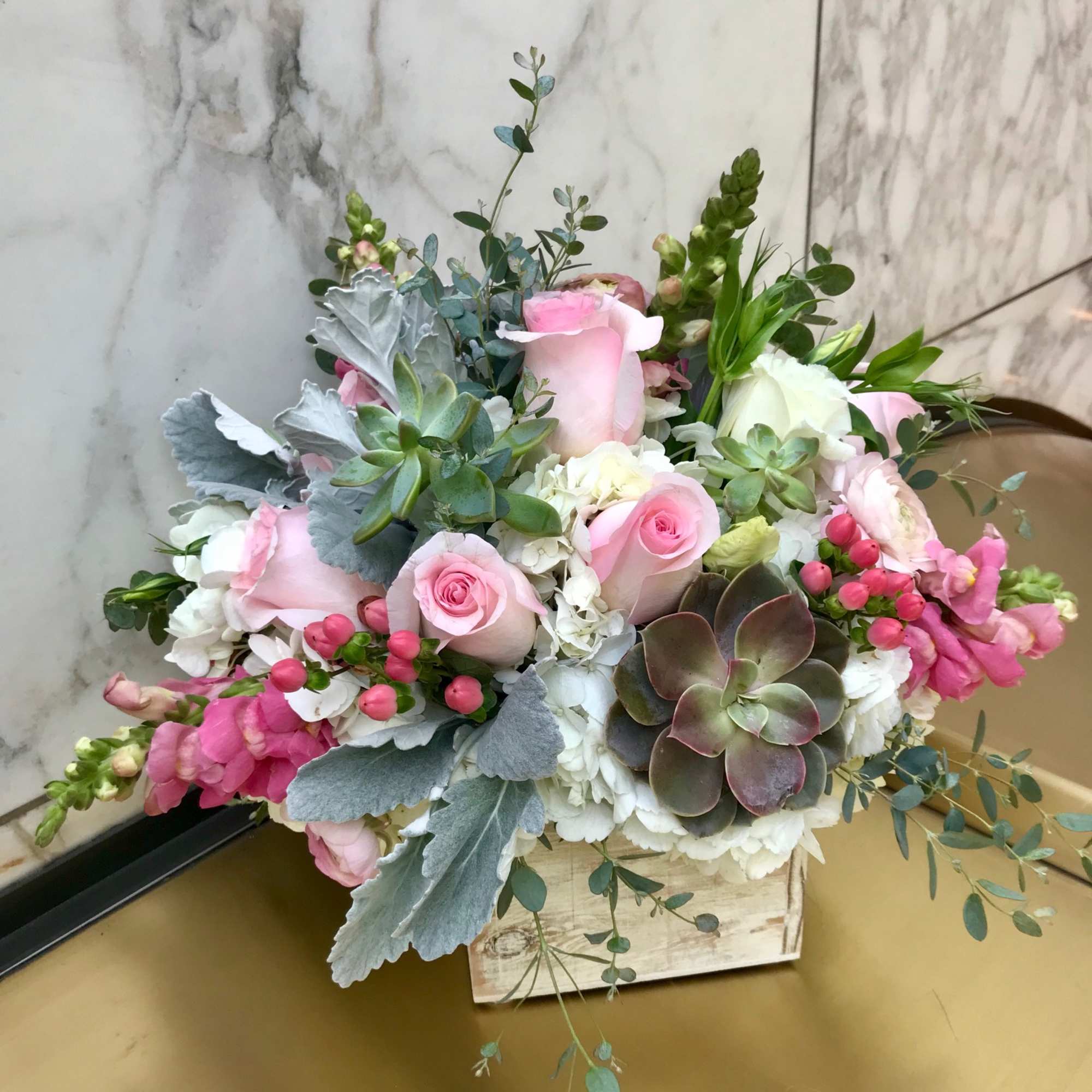 Pink roses and white blooms arranged in a wooden box with succulents