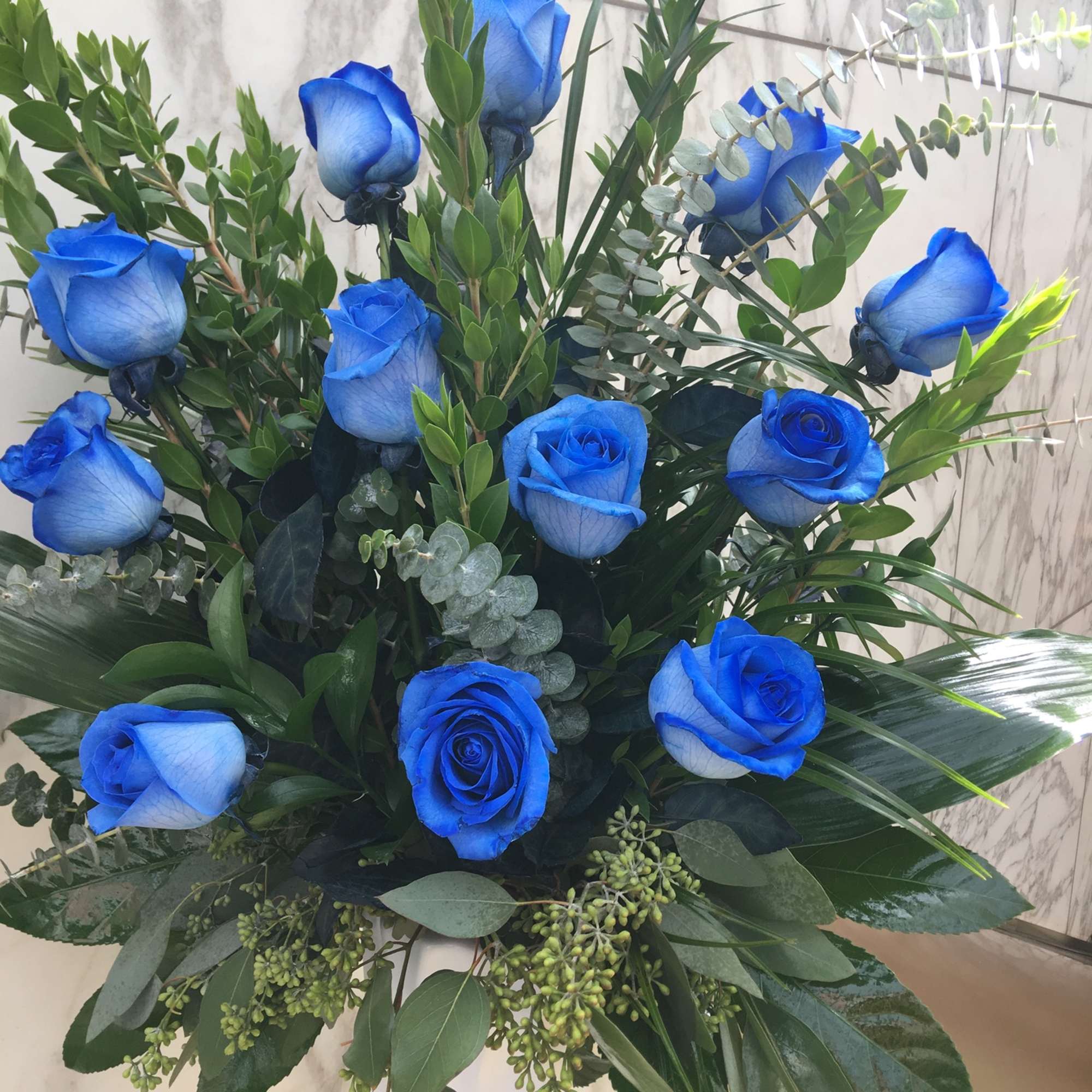 Blue roses arranged in a tall white vase with mixed greenery