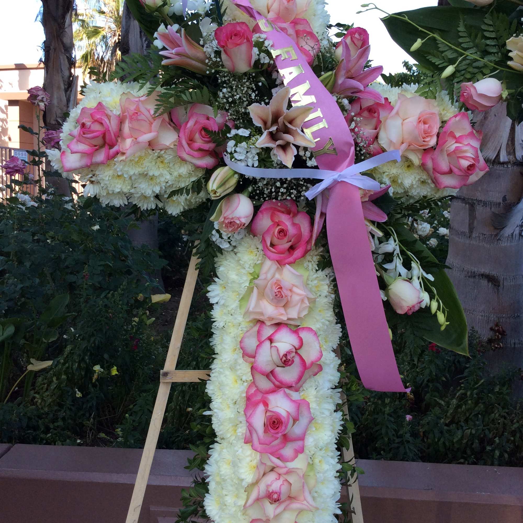 Large floral cross on an easel with pink roses and white flowers