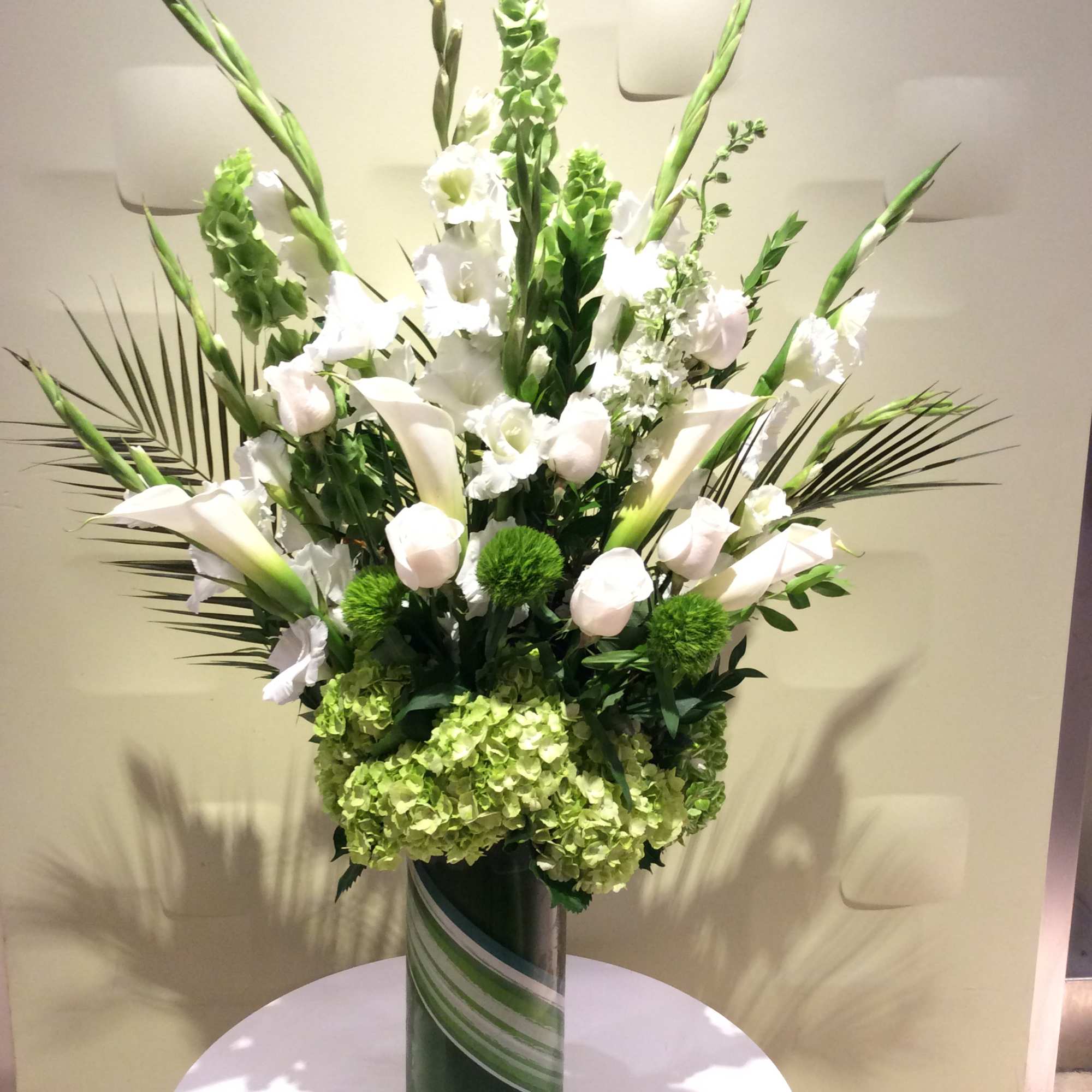 Tall white floral arrangement in a green vase with calla lilies and hydrangeas