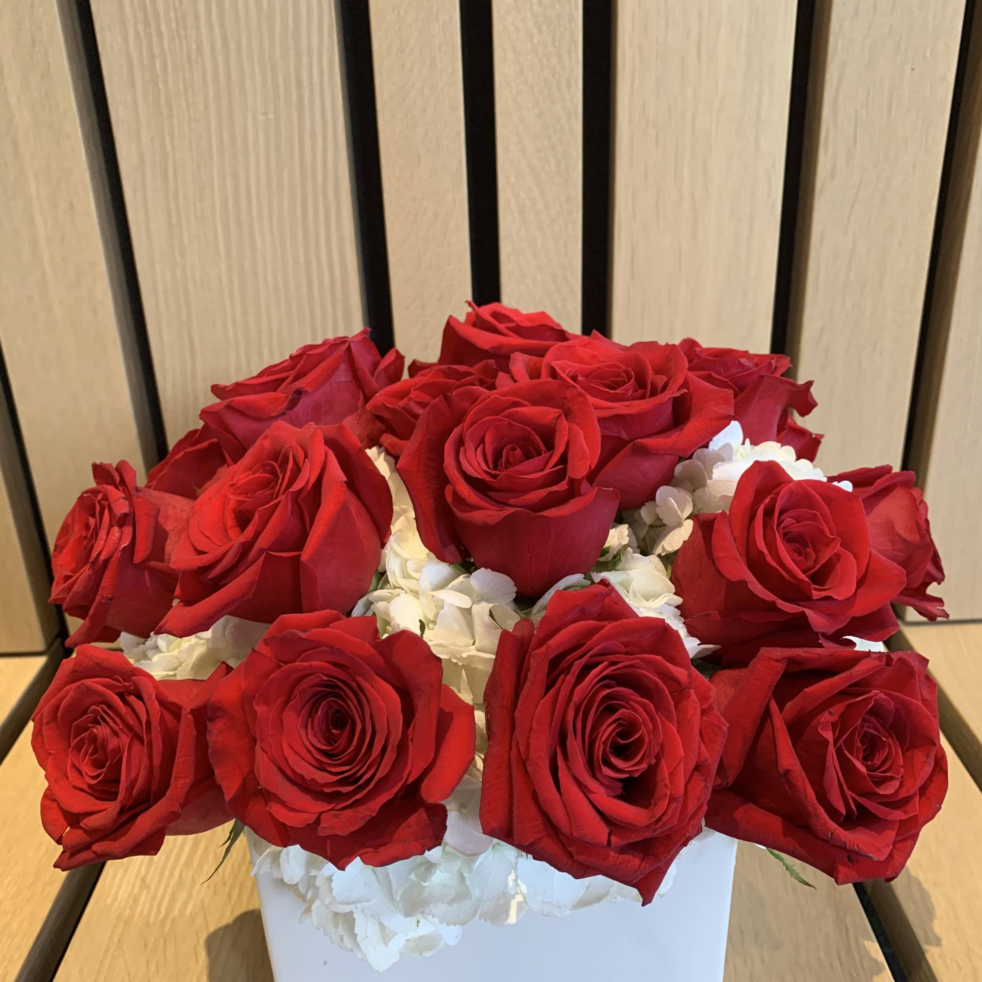 Red roses arranged in a white square box with white filler flowers
