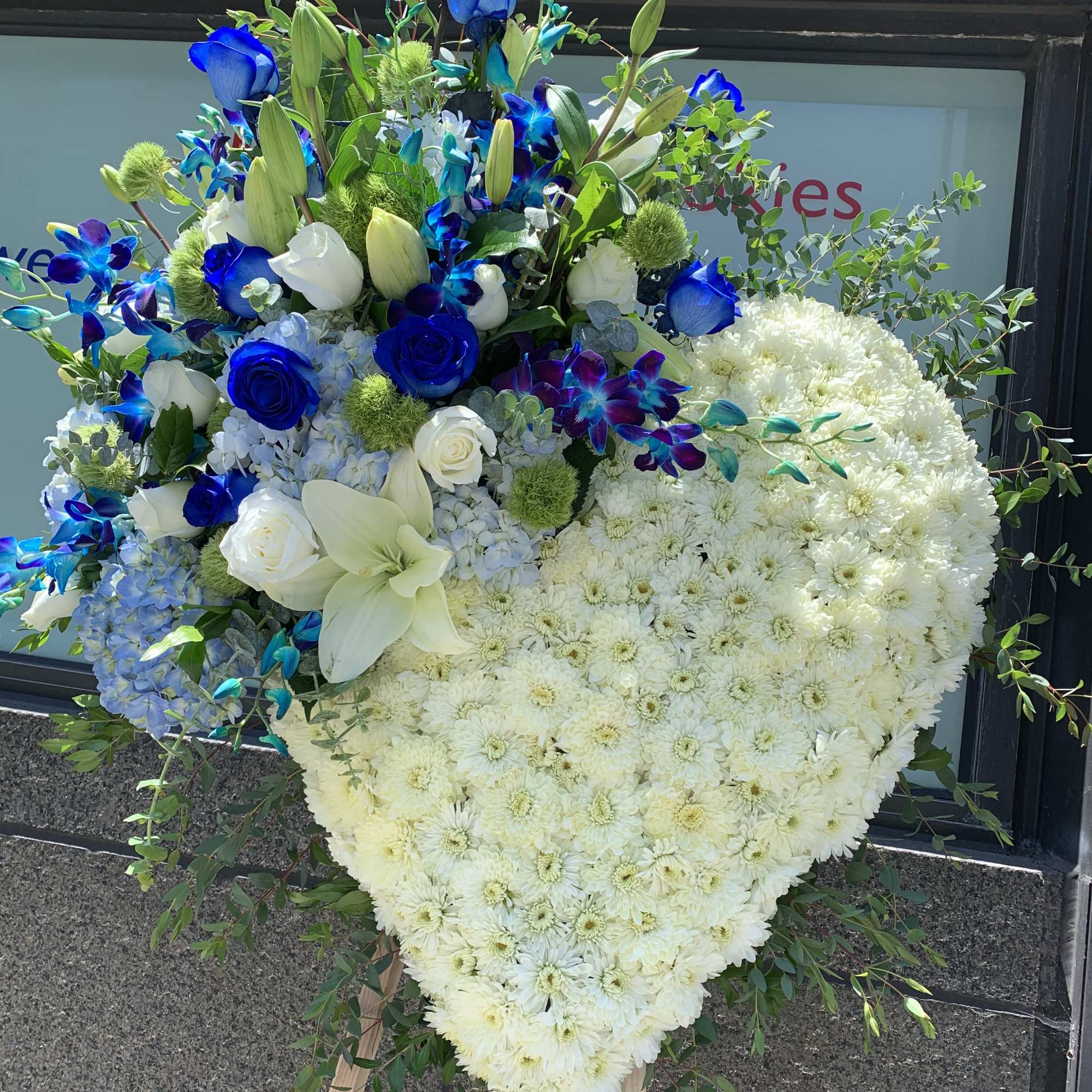 Heart-shaped white floral spray with blue roses and lilies on an easel
