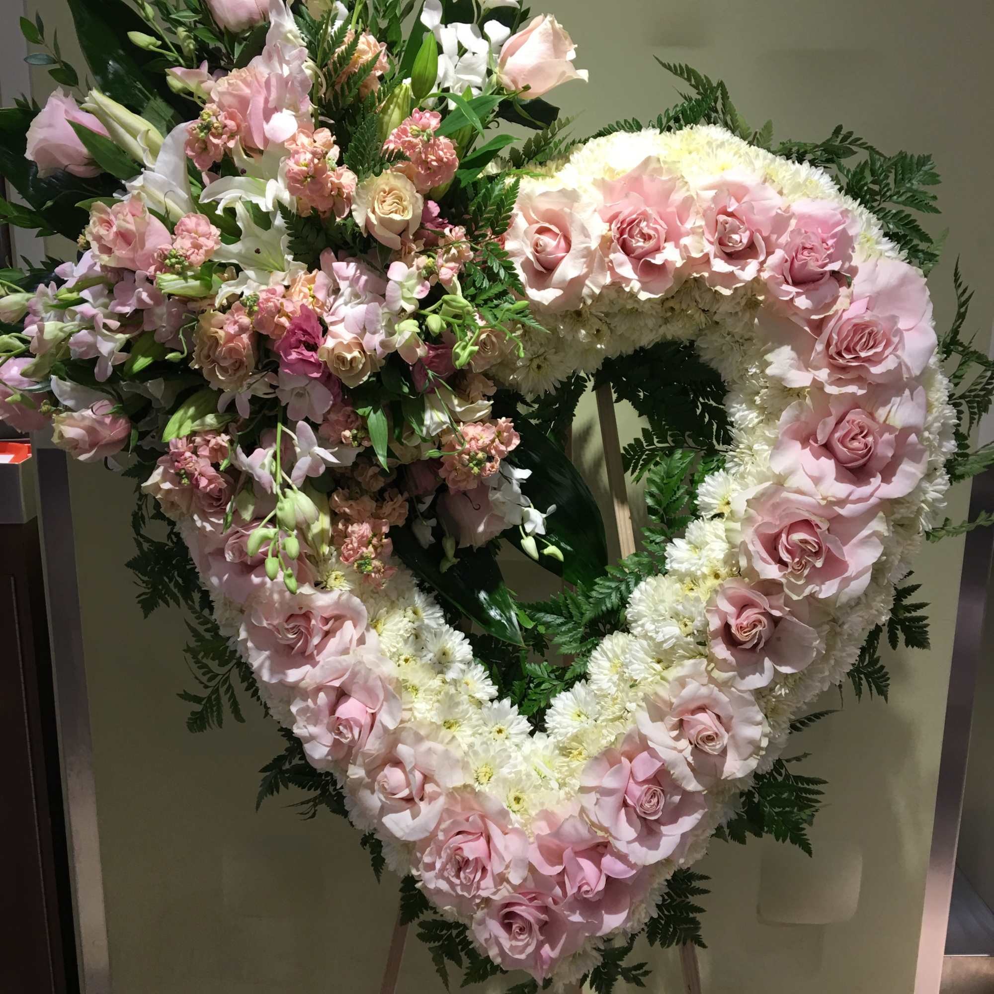 Heart-shaped floral wreath with pink roses and white flowers on an easel