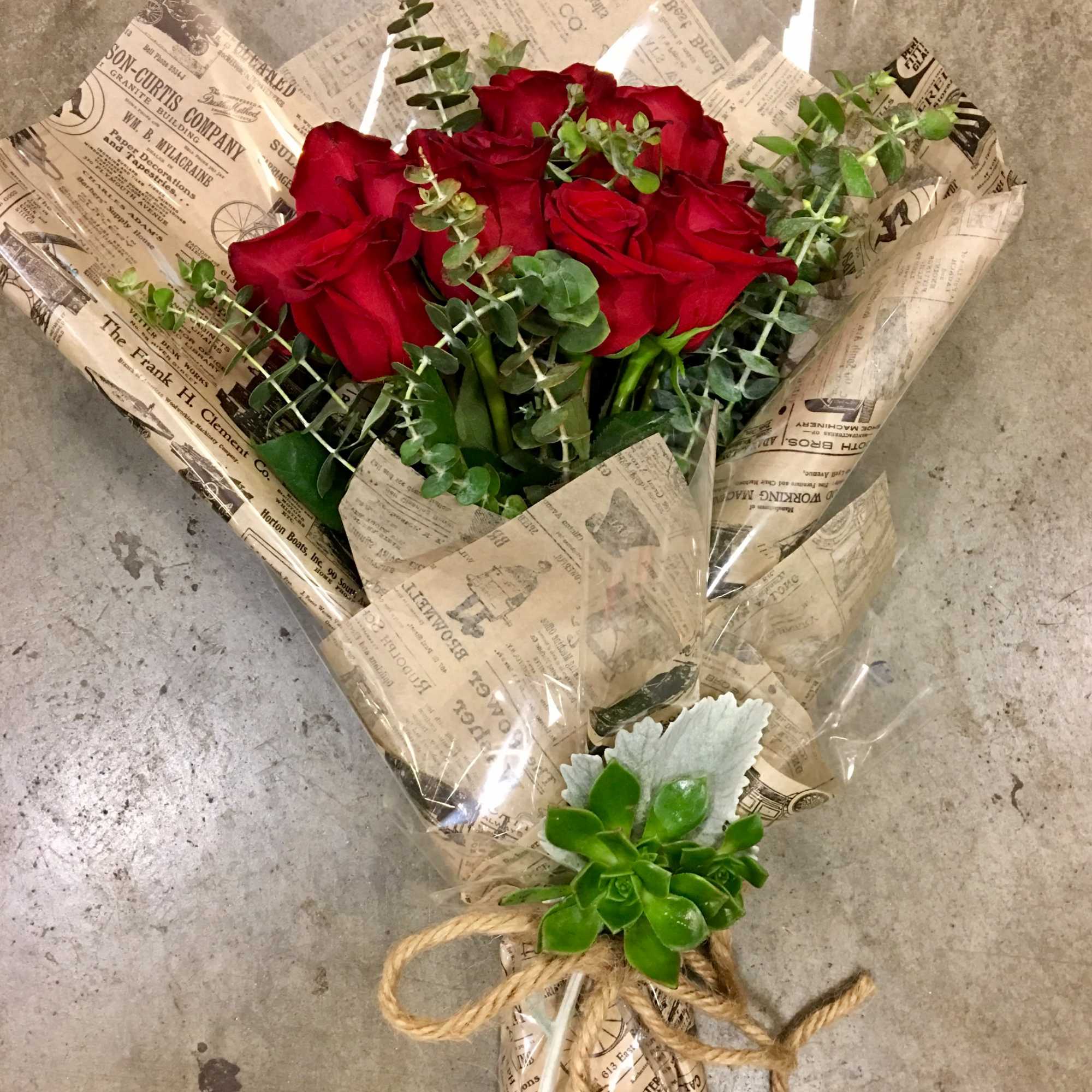 Bouquet of red roses wrapped in newspaper-style paper with eucalyptus and a succulent accent