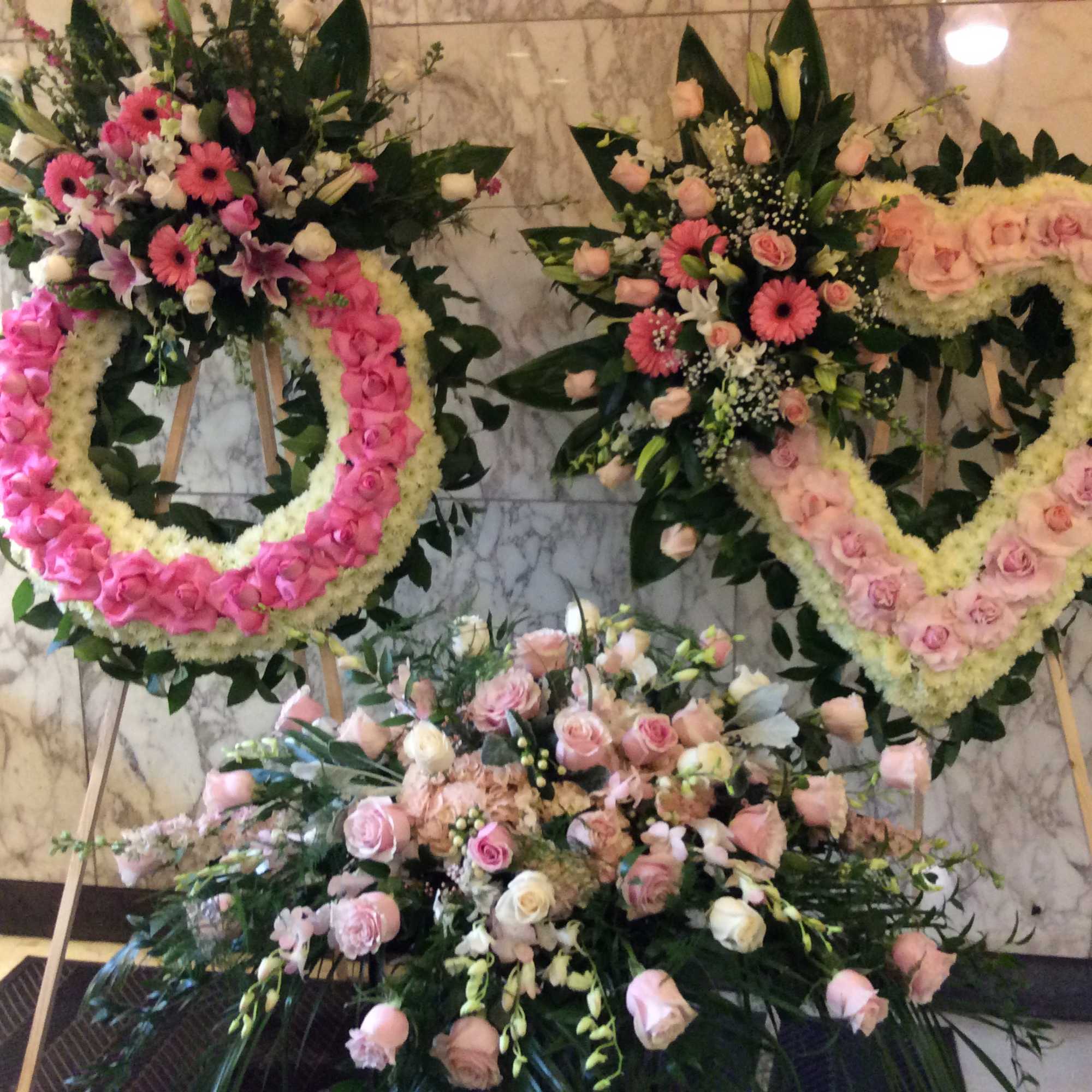 Three floral wreaths and sprays in pink and white on stands