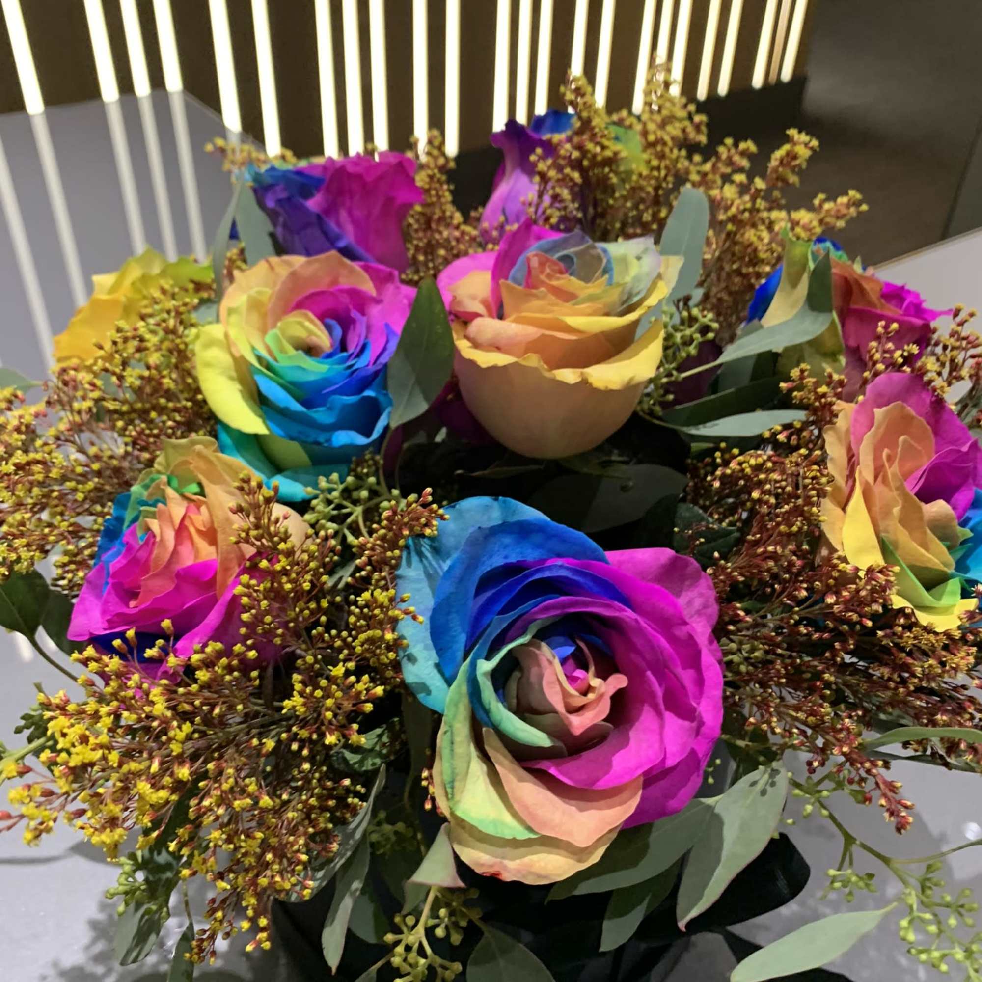 Bouquet of rainbow-colored roses with greenery and filler flowers
