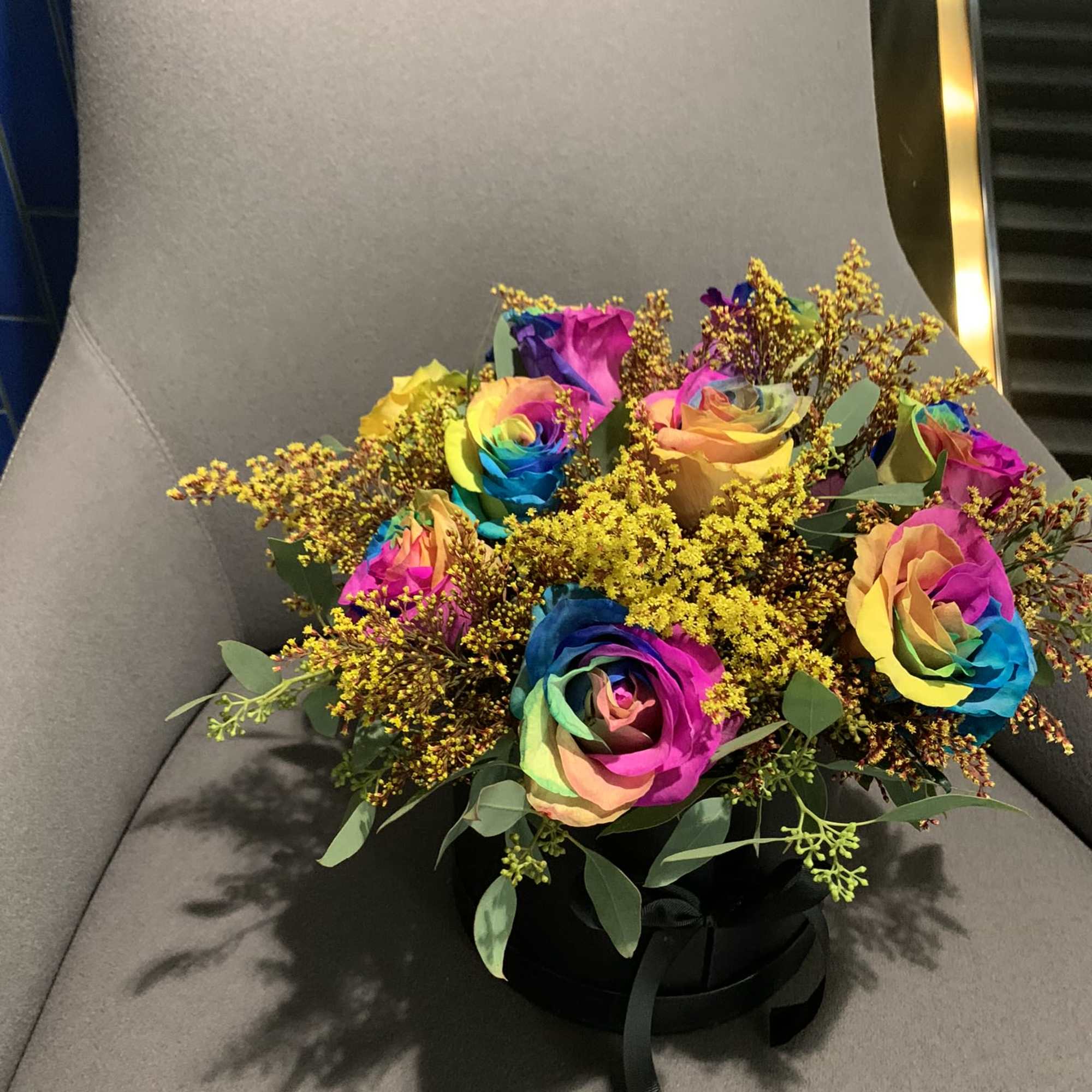 Rainbow roses arranged in a black hatbox with yellow filler flowers