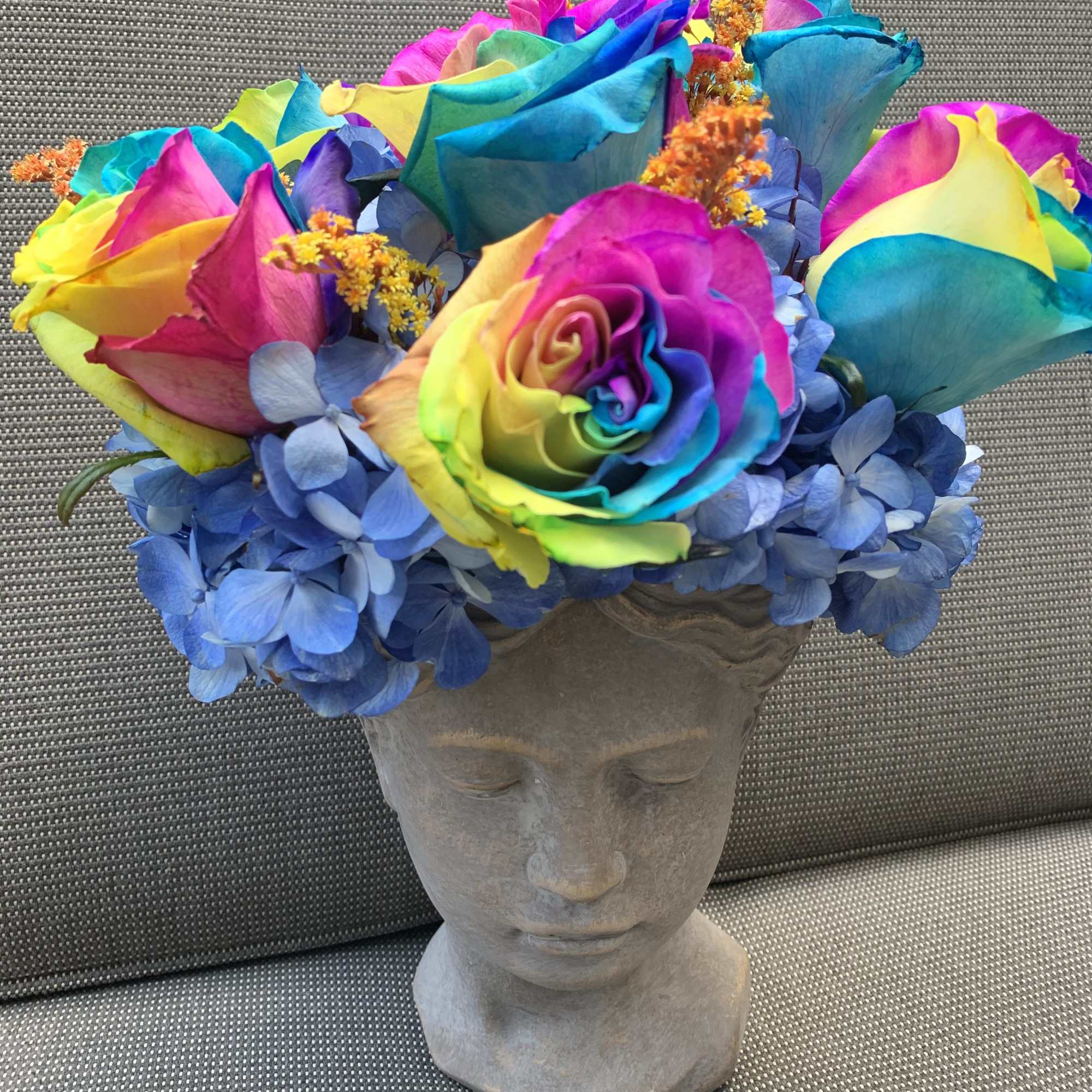 Rainbow roses and blue hydrangeas arranged in a stone head planter