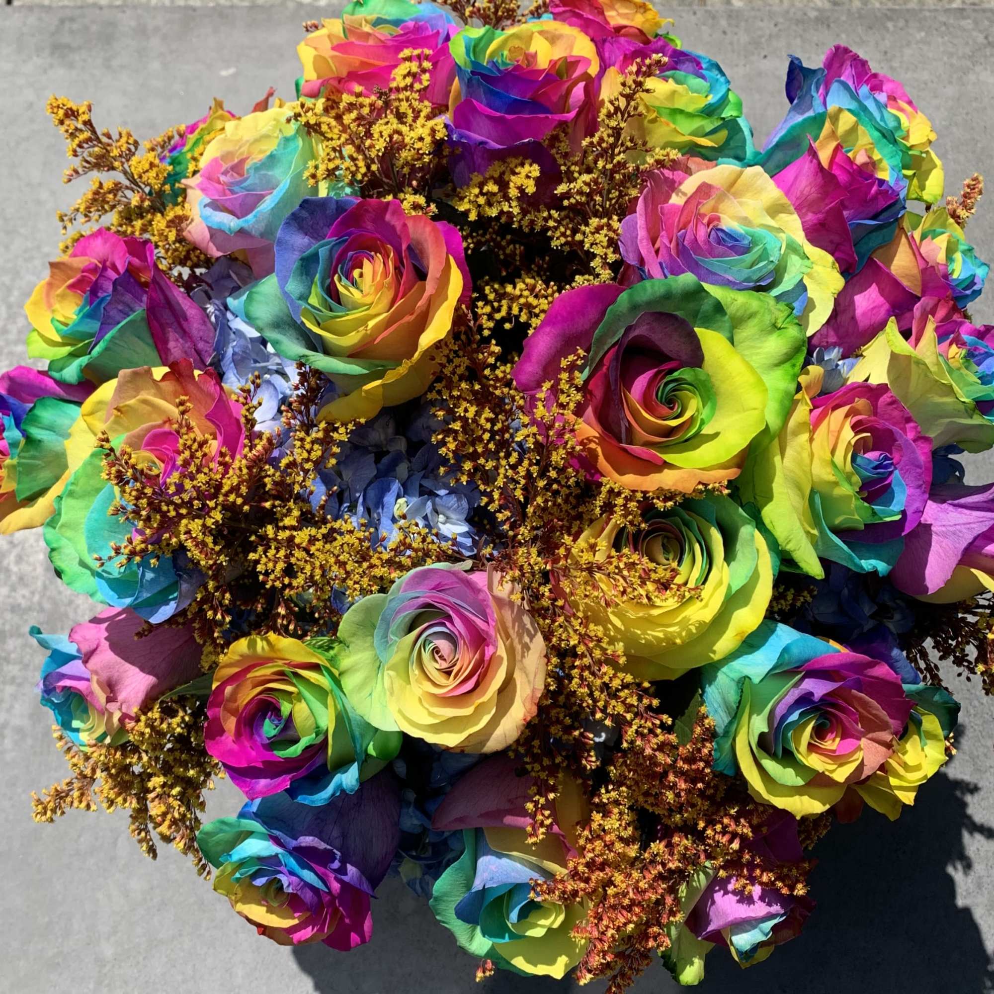 Bouquet of rainbow-colored roses with small yellow filler flowers