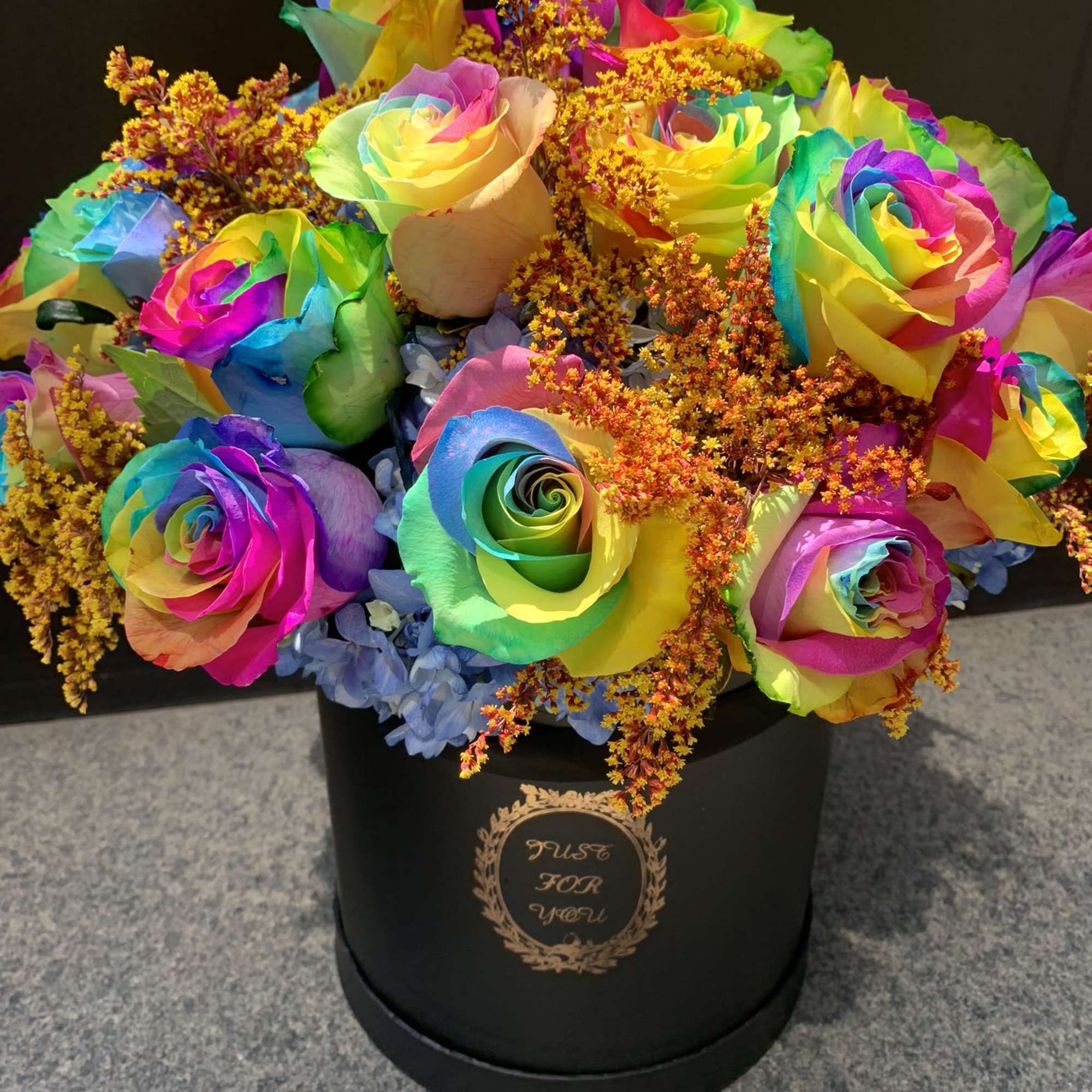 Rainbow roses in a black hatbox with orange filler flowers