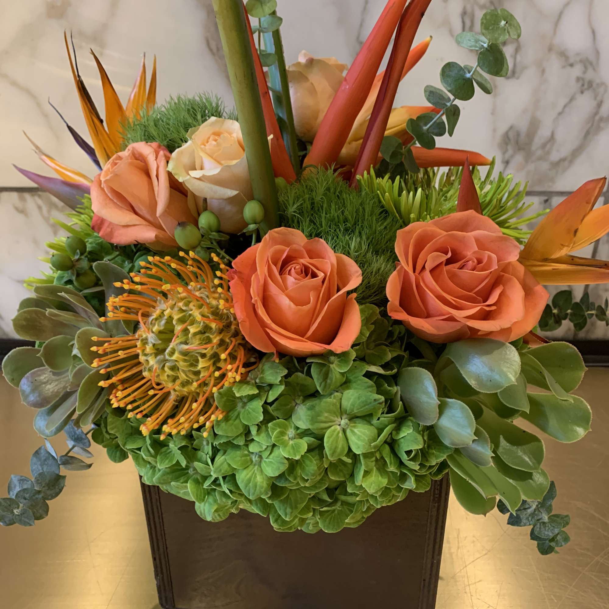 Orange roses and tropical flowers in a square black vase