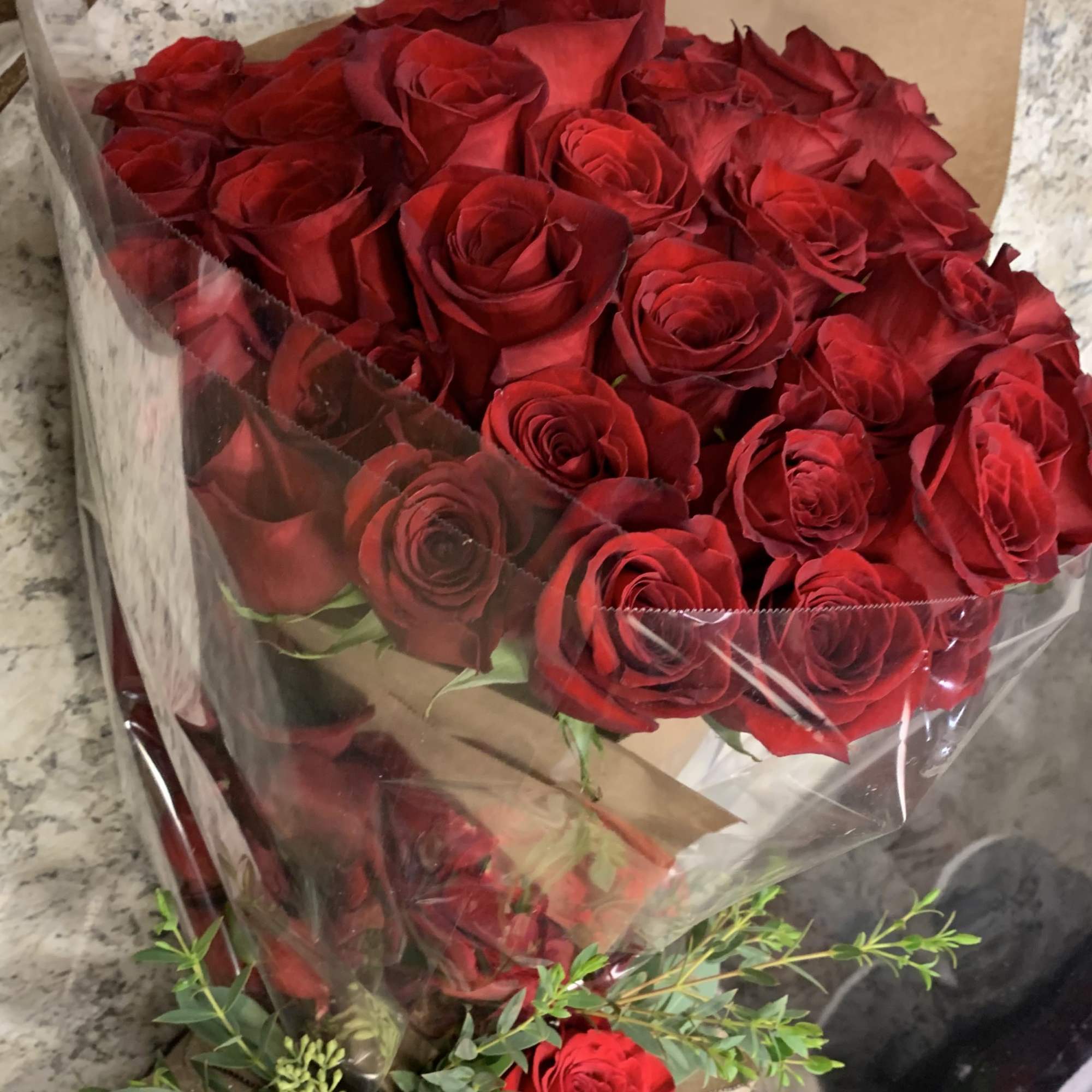Bouquet of red roses wrapped in clear plastic with greenery