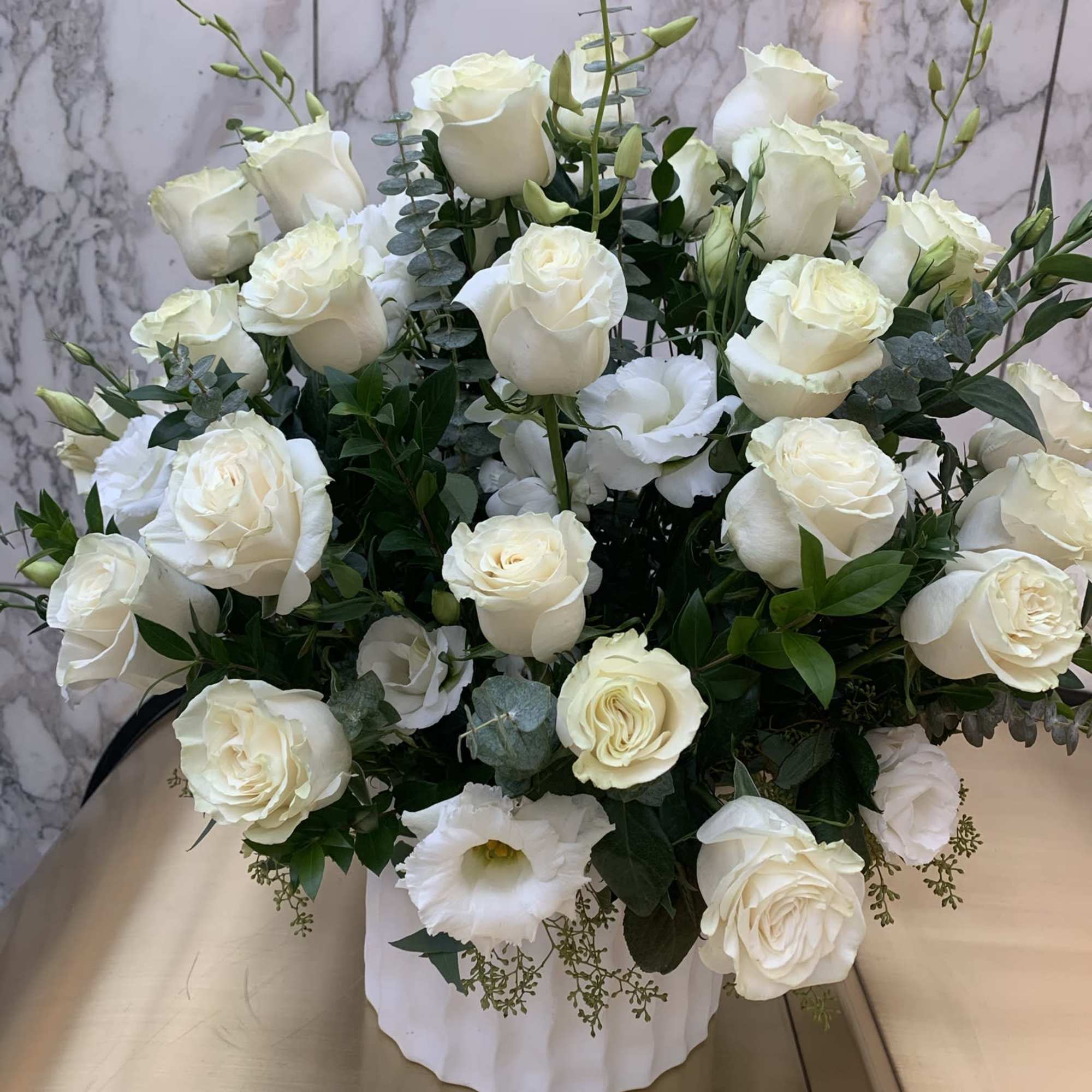 White rose arrangement in a white vase with eucalyptus accents
