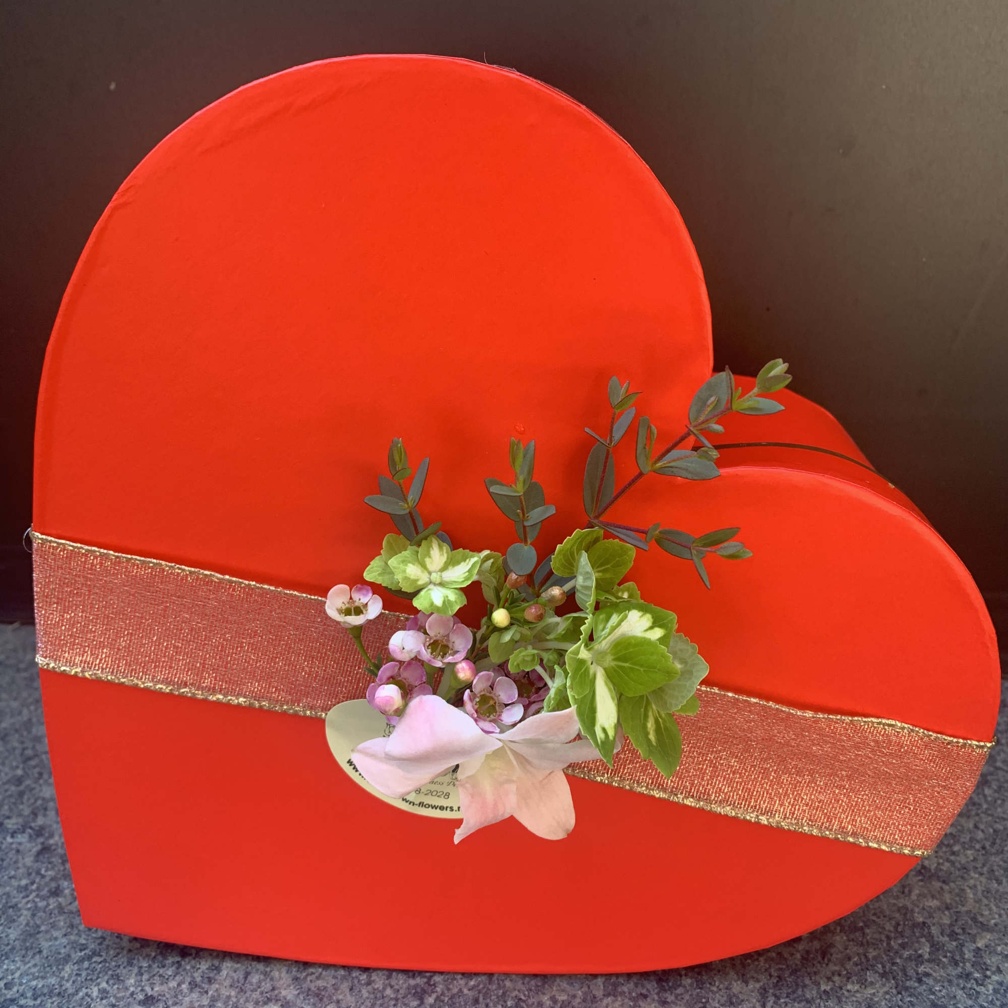 Red heart-shaped gift box with a small floral accent and ribbon