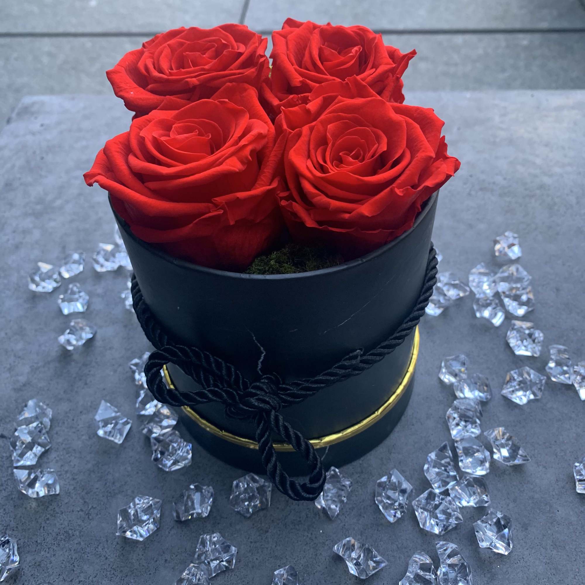 Four red roses in a black round box with clear decorative crystals