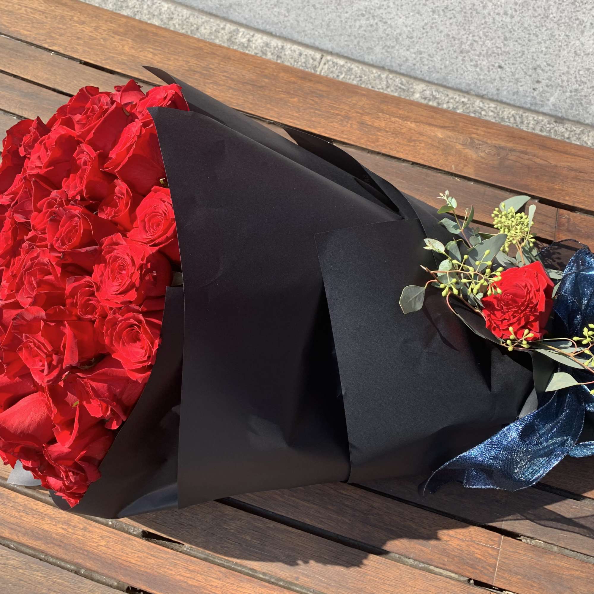 Bouquet of red roses wrapped in black paper with a blue ribbon