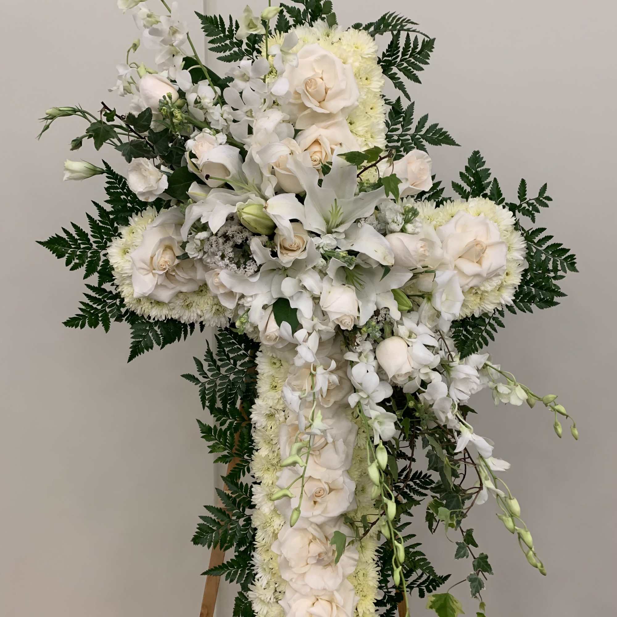 White floral cross arrangement with roses and lilies on an easel