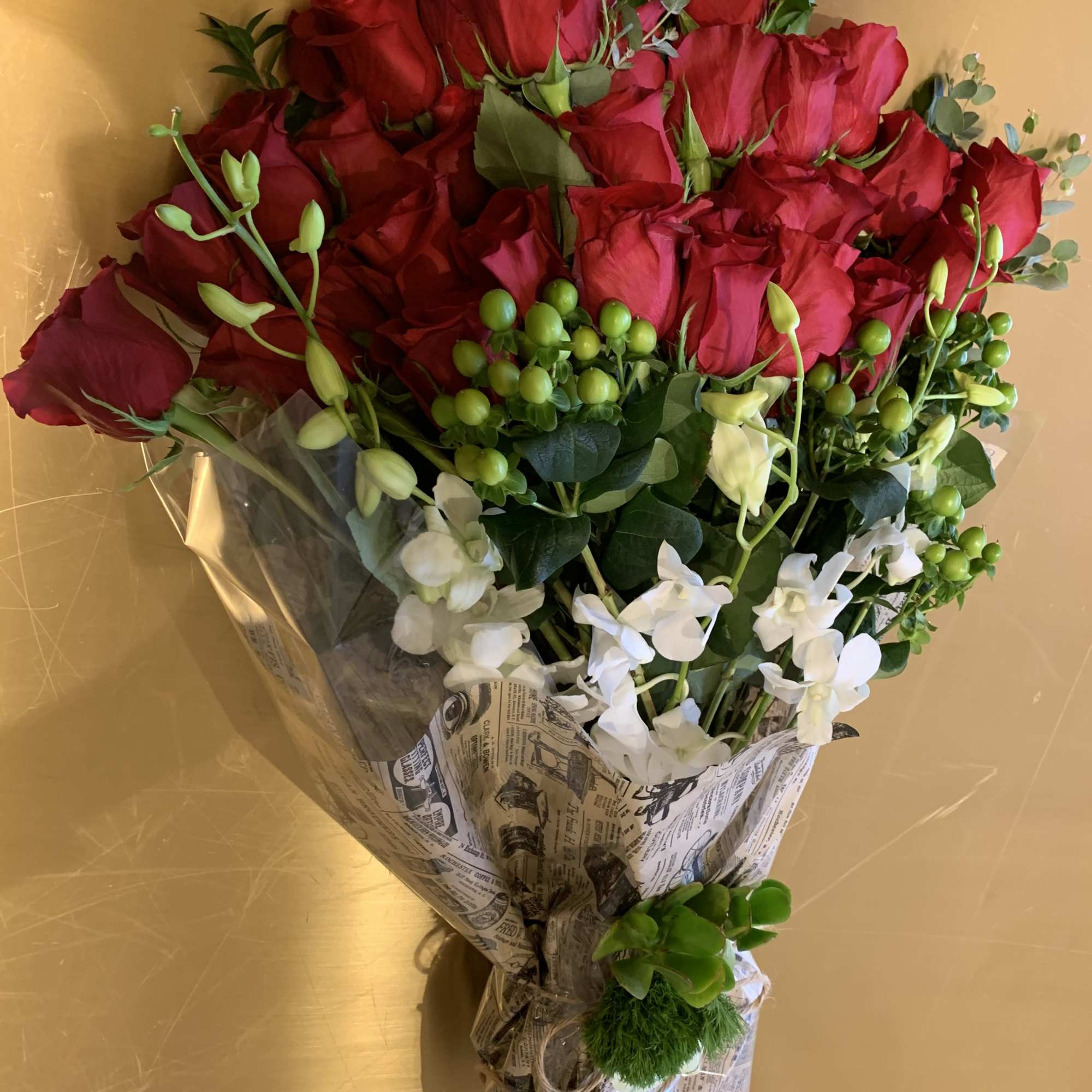 Bouquet of red roses with white orchids and green berries in paper wrap