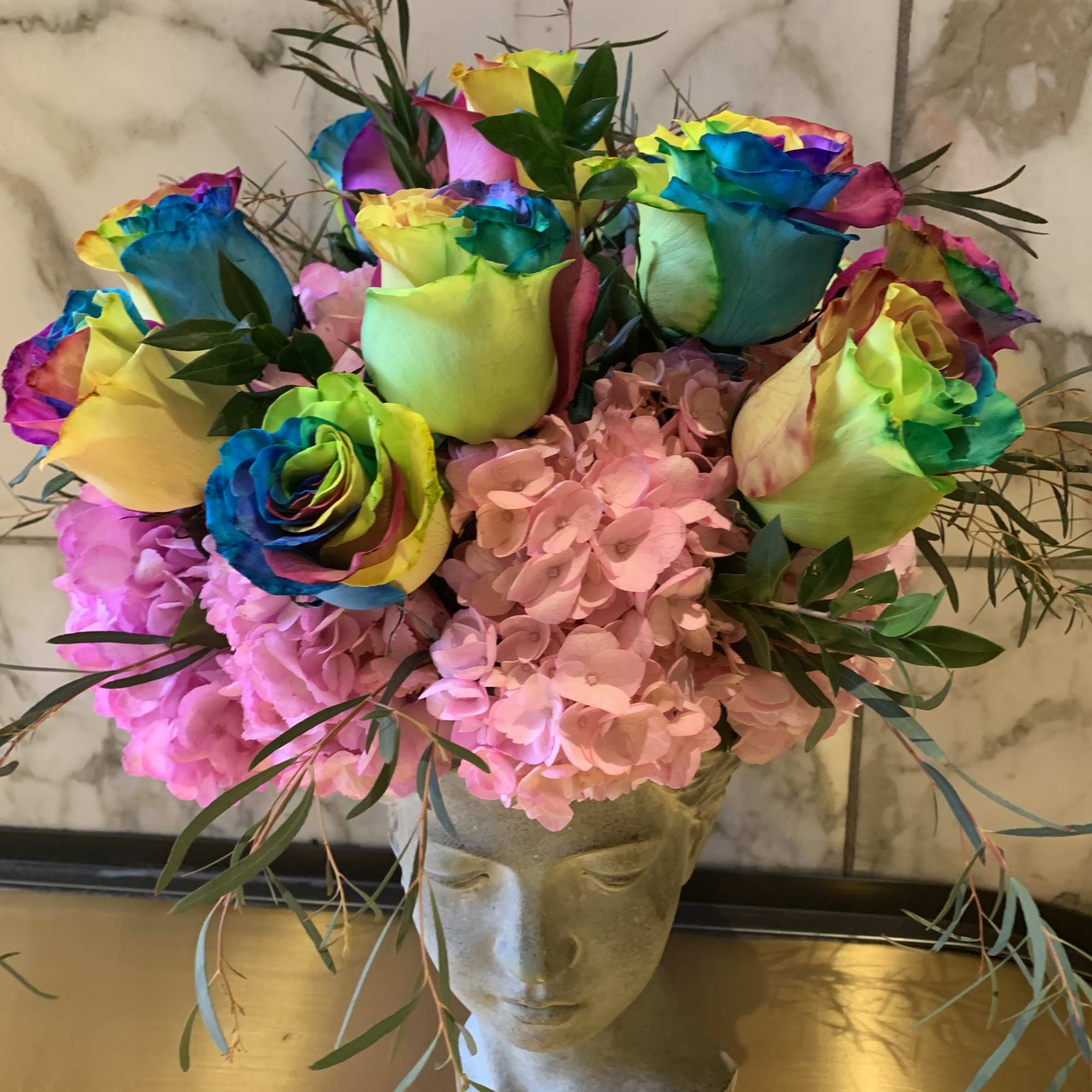 Rainbow roses and pink hydrangeas in a sculpted face vase