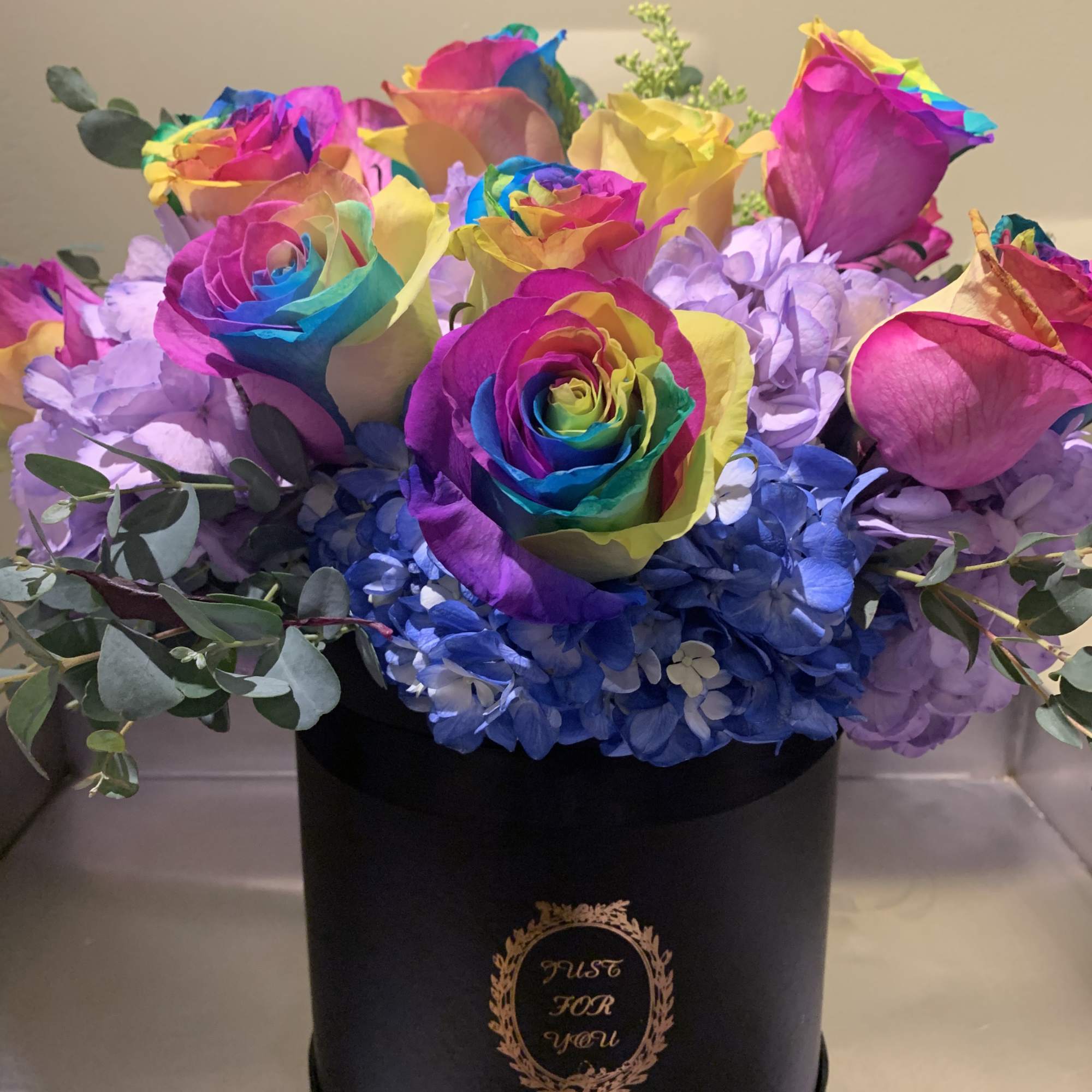 Rainbow-colored roses in a black hatbox with blue hydrangeas