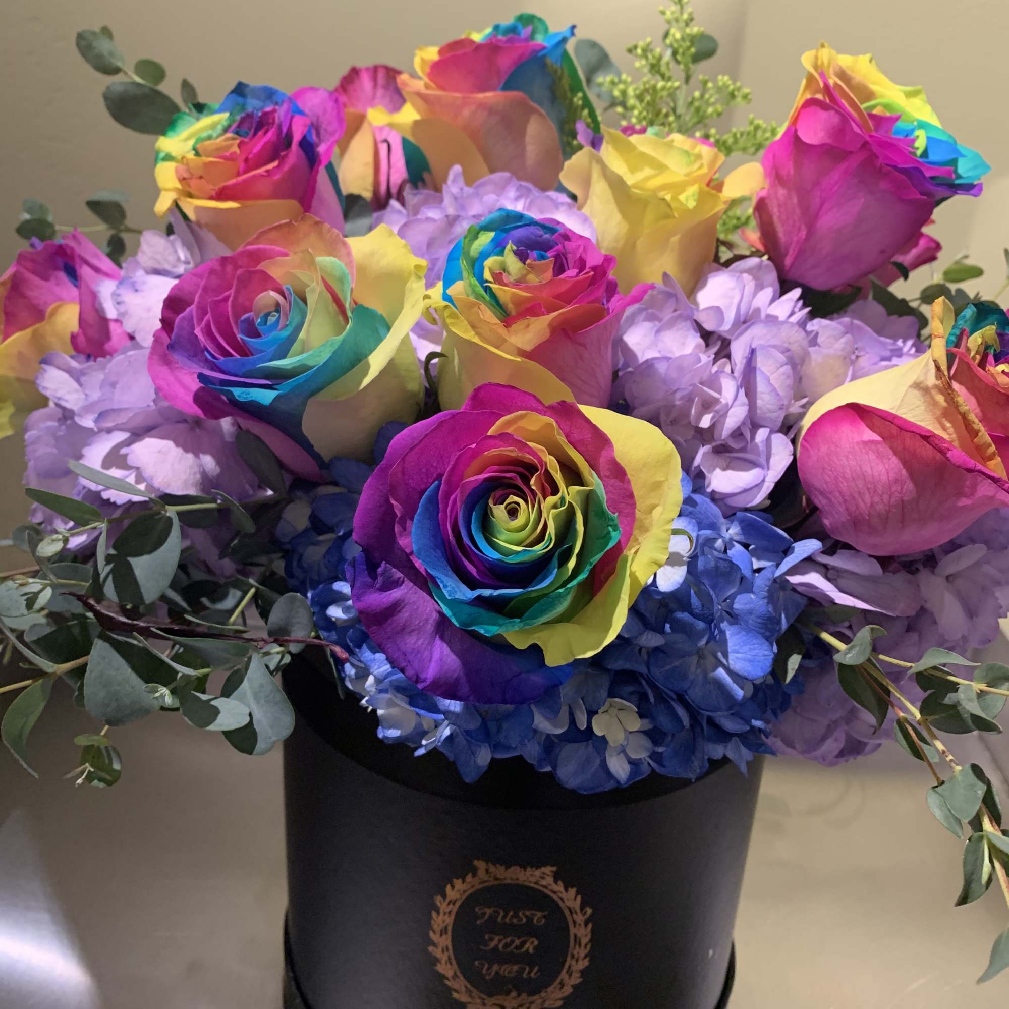 Rainbow-colored roses in a black hat box with blue hydrangeas