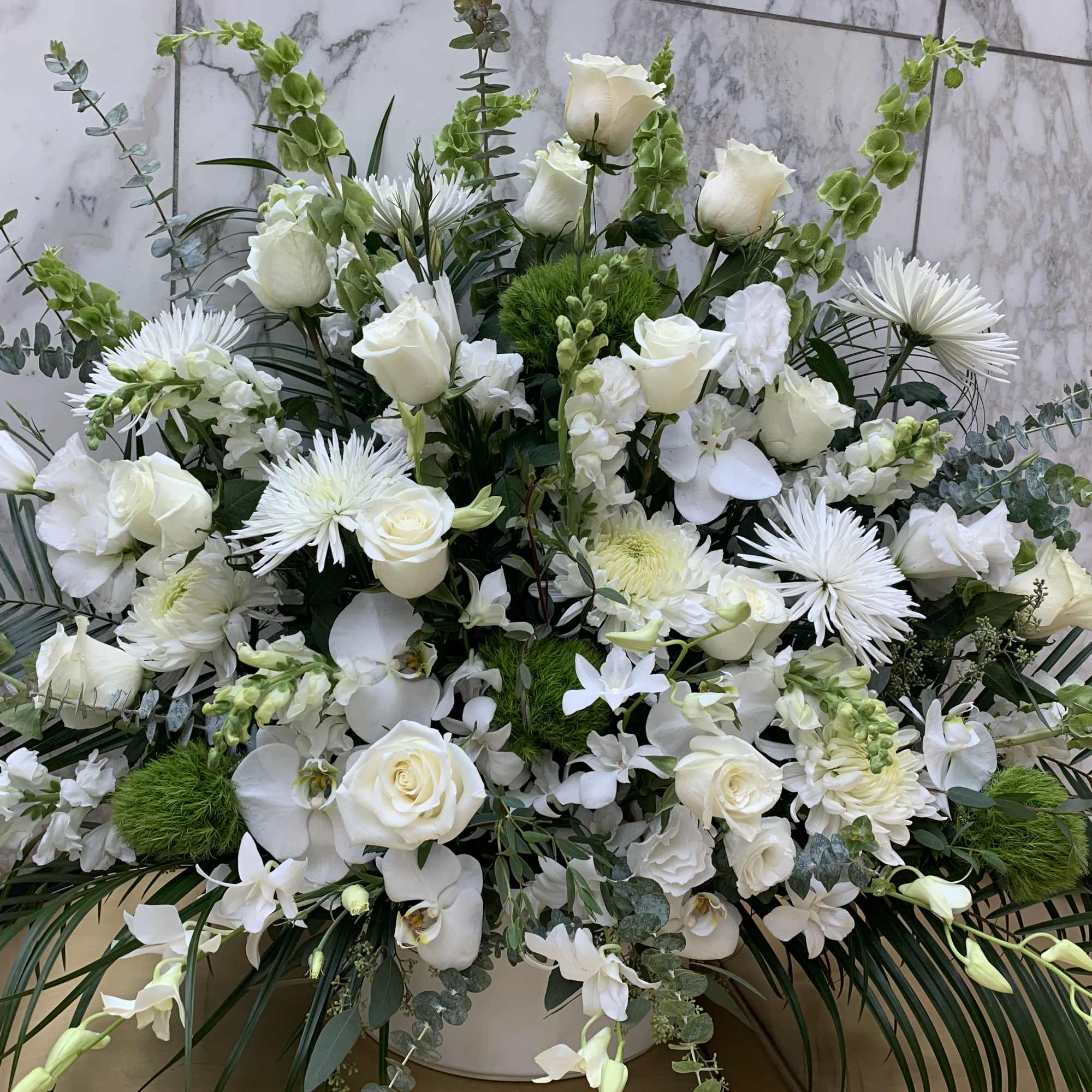 Large white floral arrangement with roses and orchids in a white container