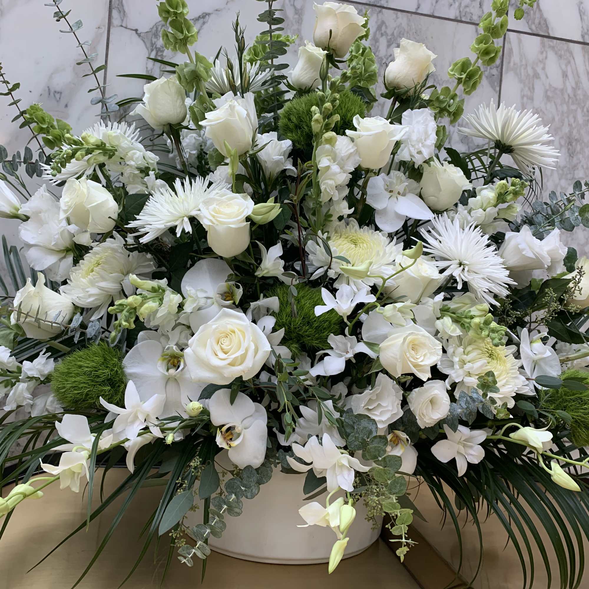 White floral arrangement in a low white container with roses and orchids
