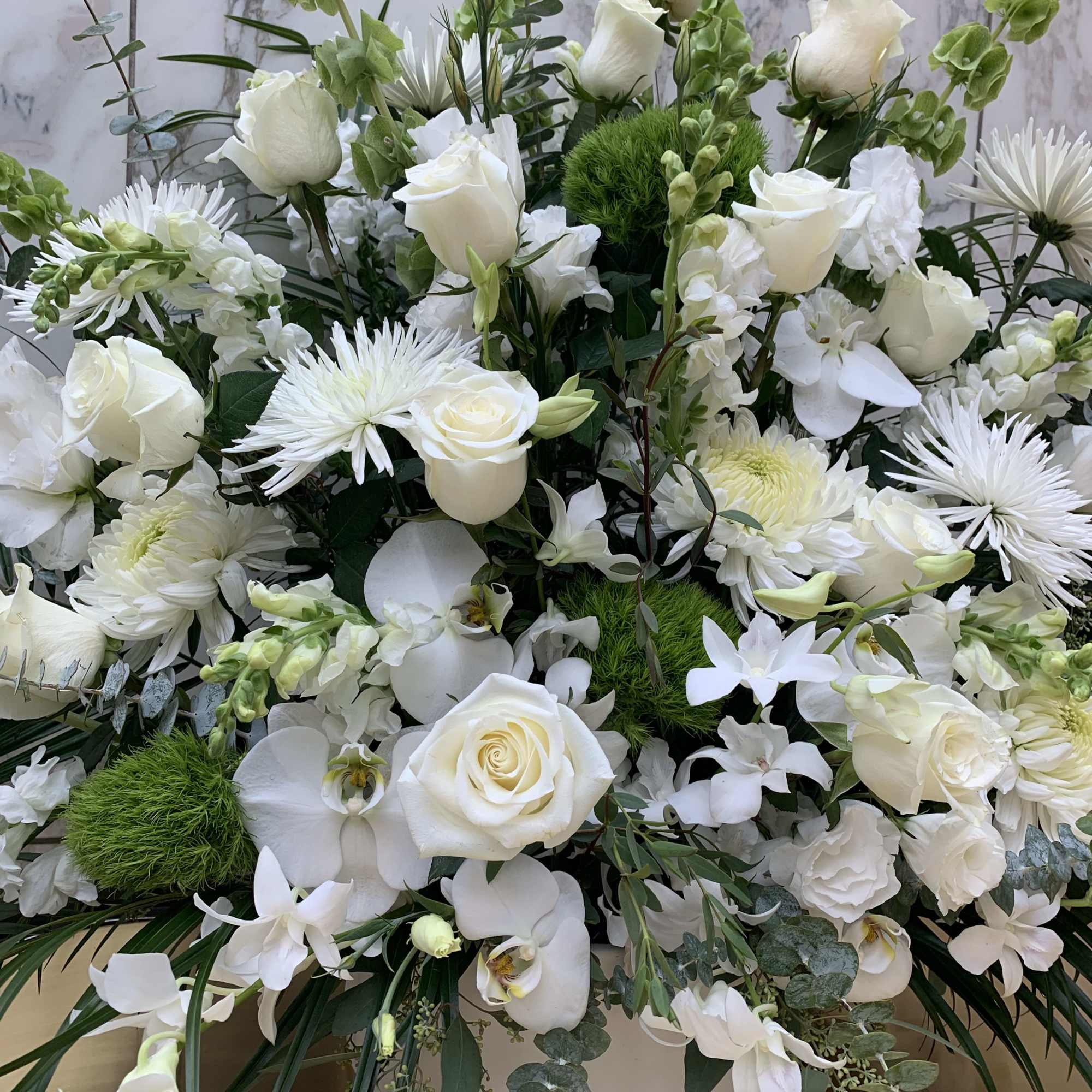 White roses and orchids arranged with green accents in a low container