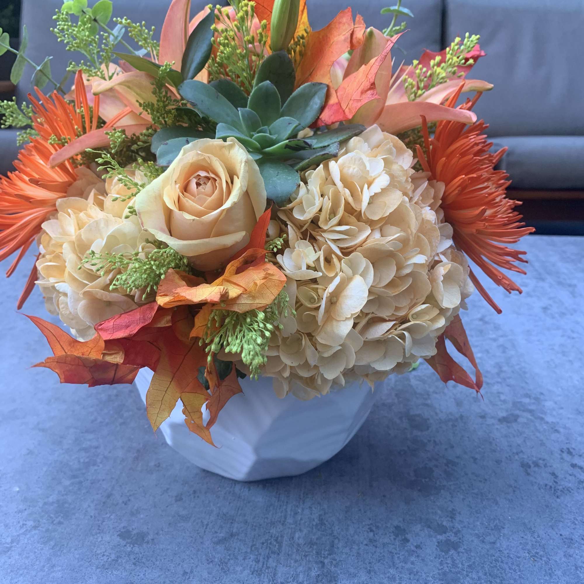 Bouquet of peach roses, cream hydrangeas, and orange flowers in a white vase