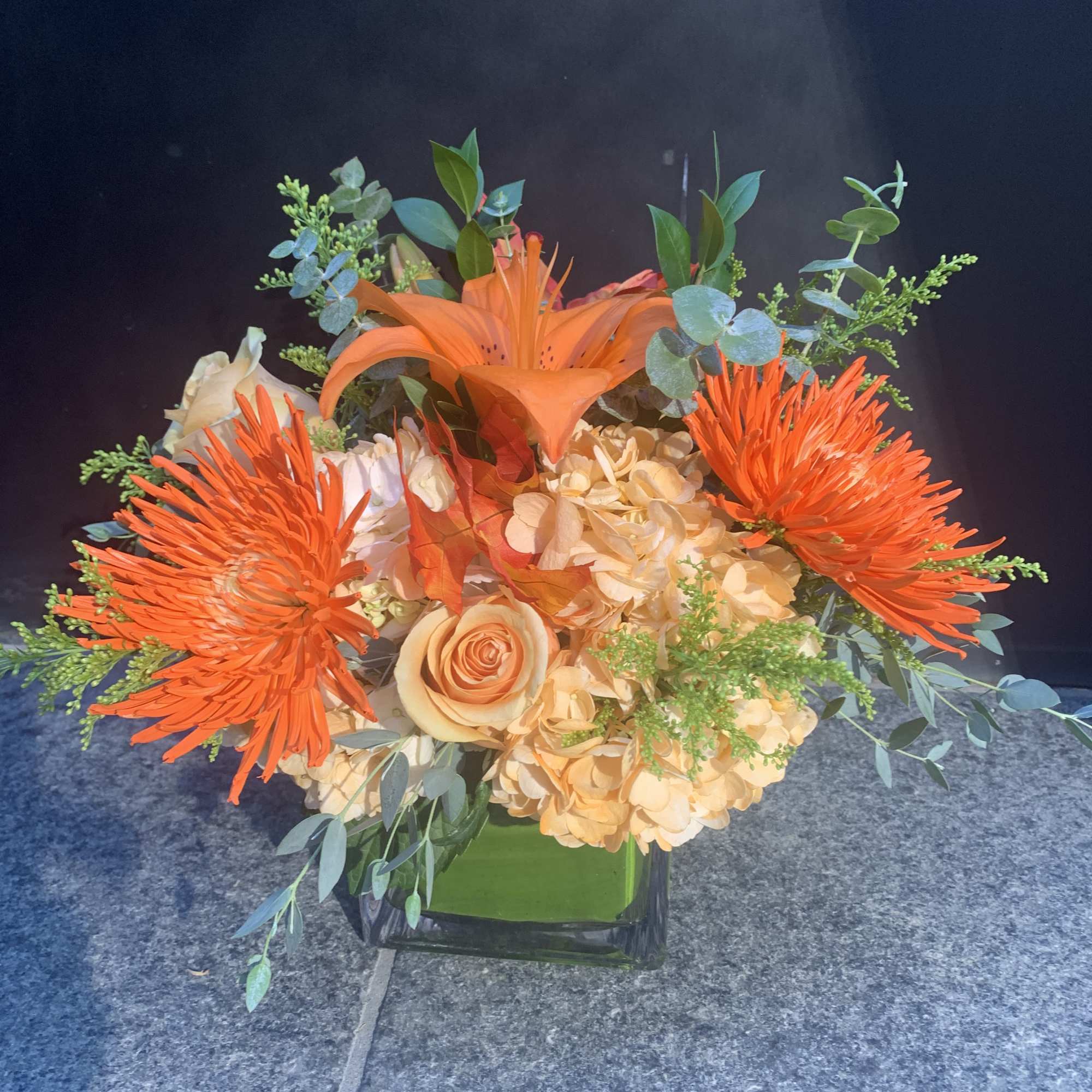 Orange lilies and chrysanthemums in a glass vase with peach roses