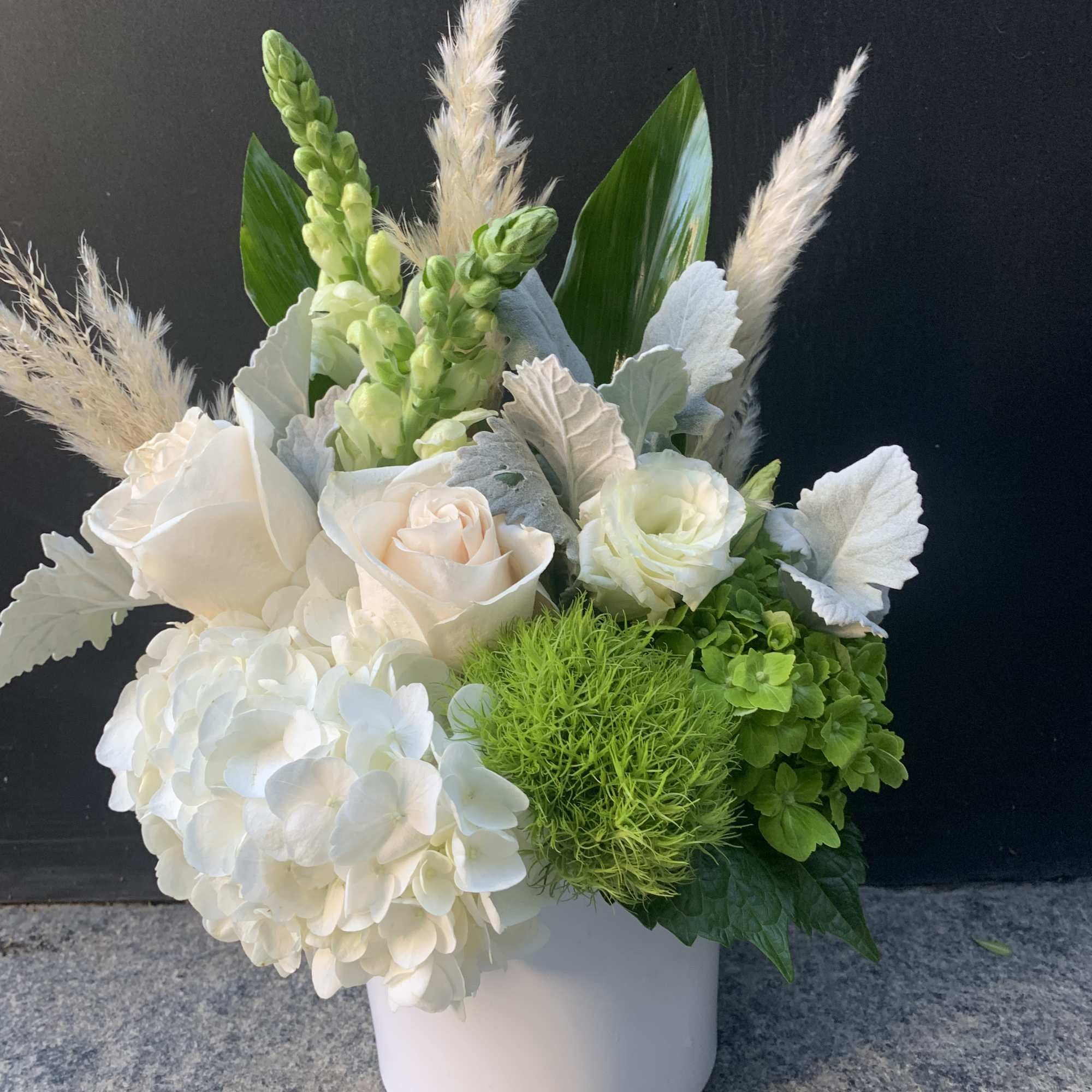 White floral arrangement in a white vase with green accents