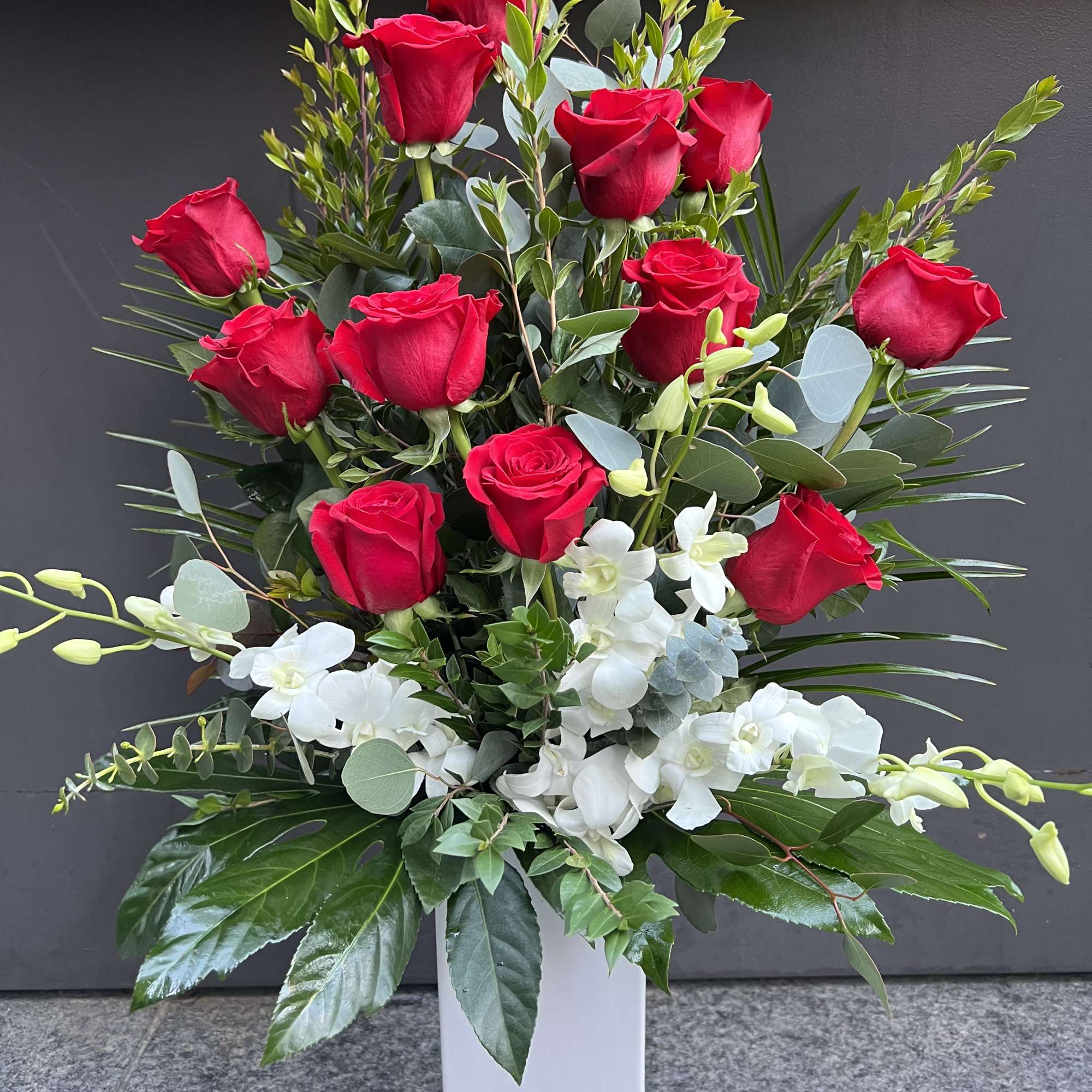 Tall arrangement of red roses and white orchids in a white vase