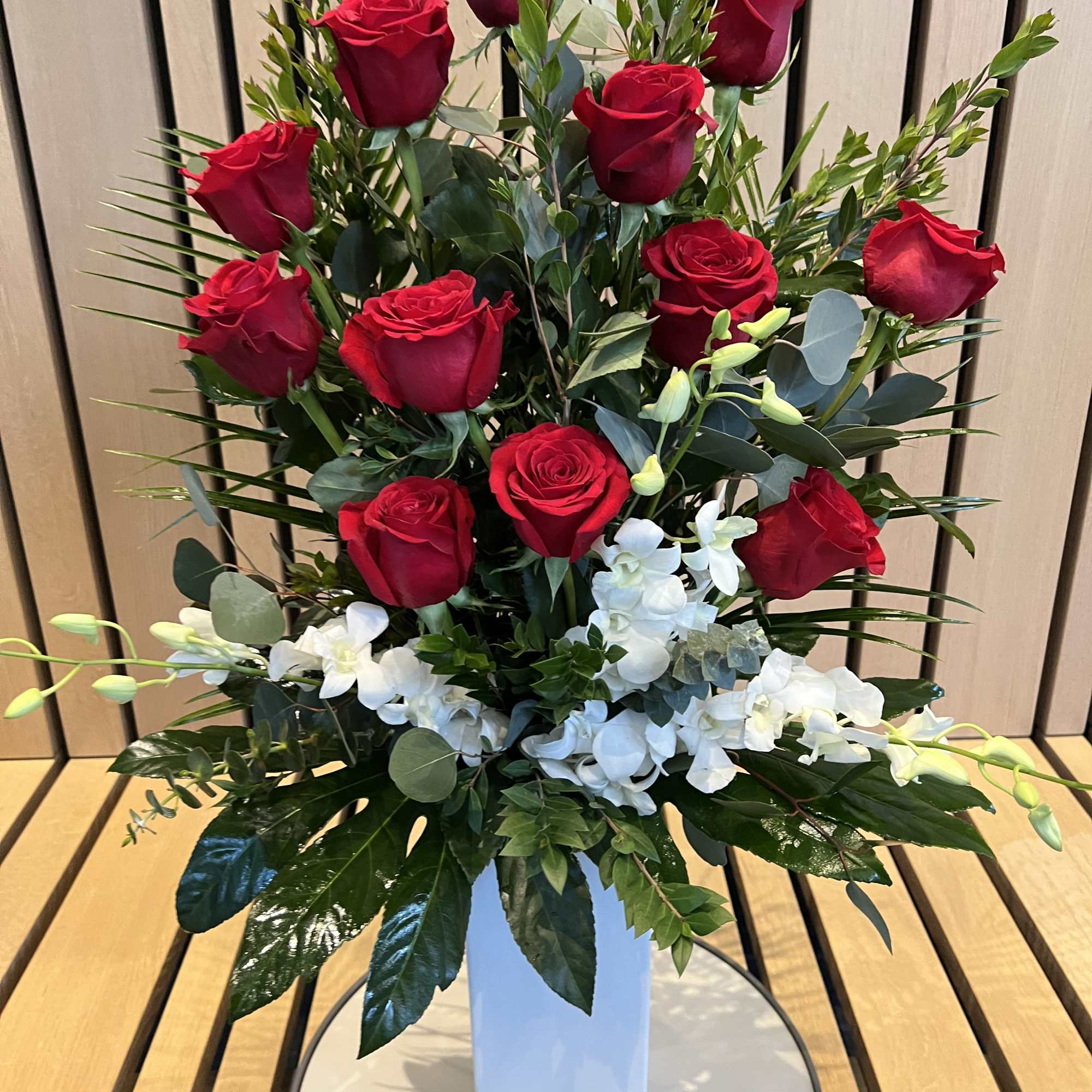 Tall bouquet of red roses and white orchids in a white vase