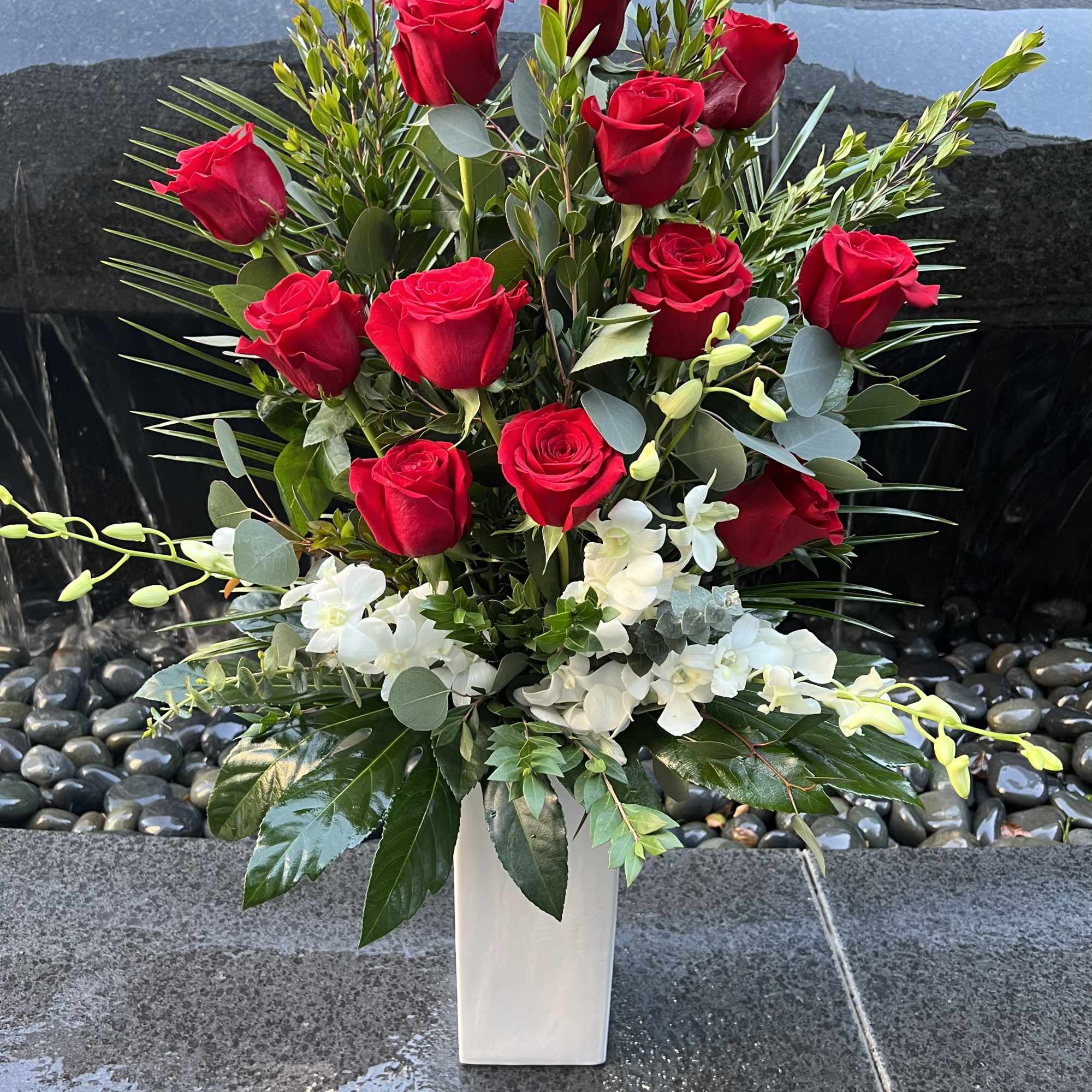 Red roses and white orchids in a tall white vase