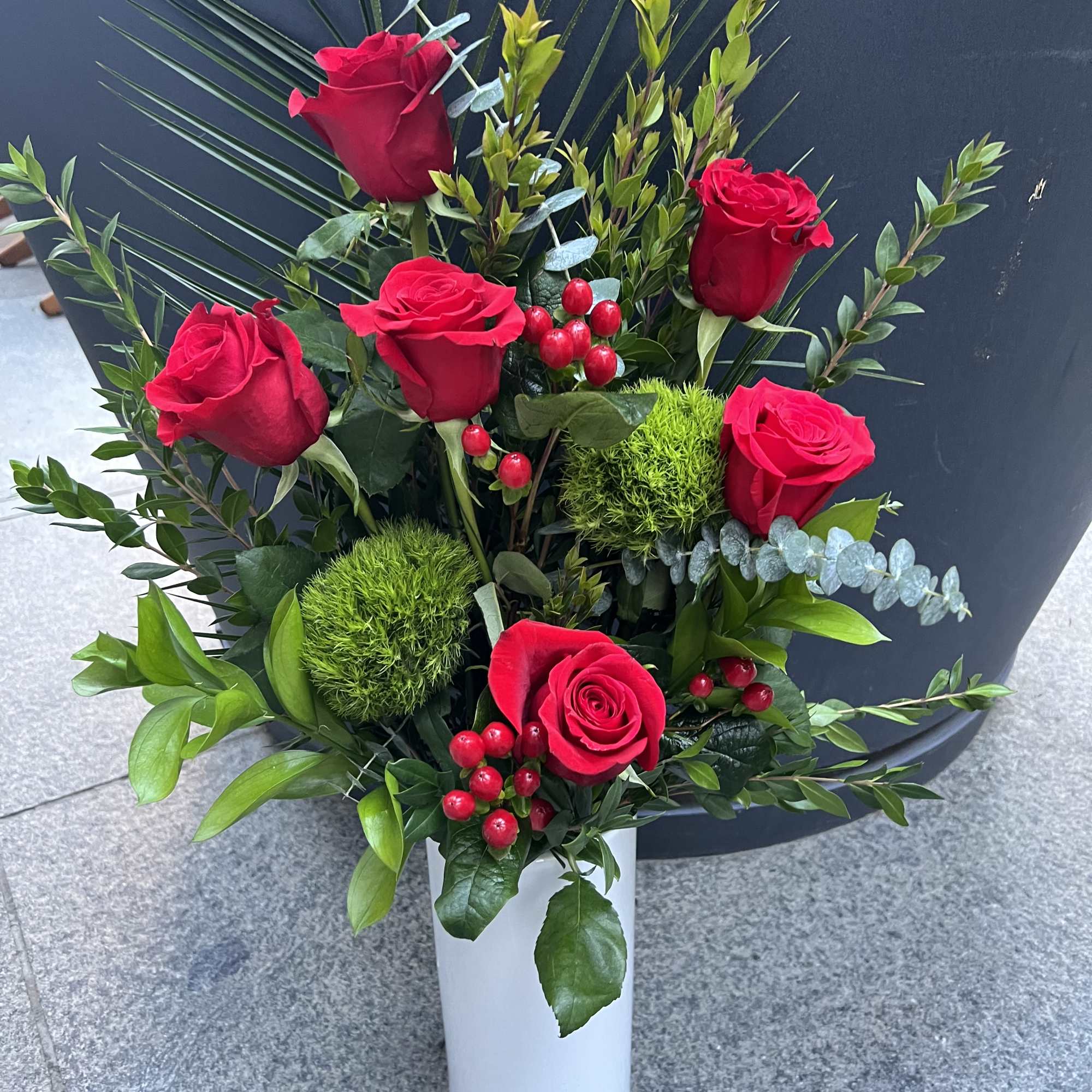 Red roses arranged in a white vase with greenery and red berries, photo 2 of 4