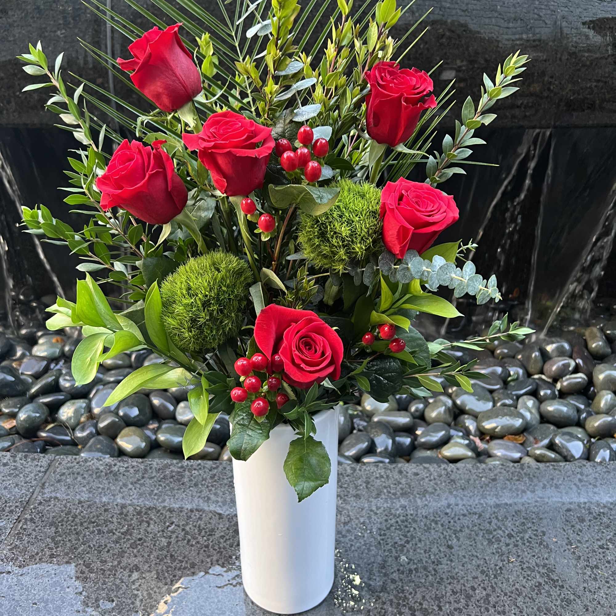 Red roses arranged in a white vase with mixed greenery