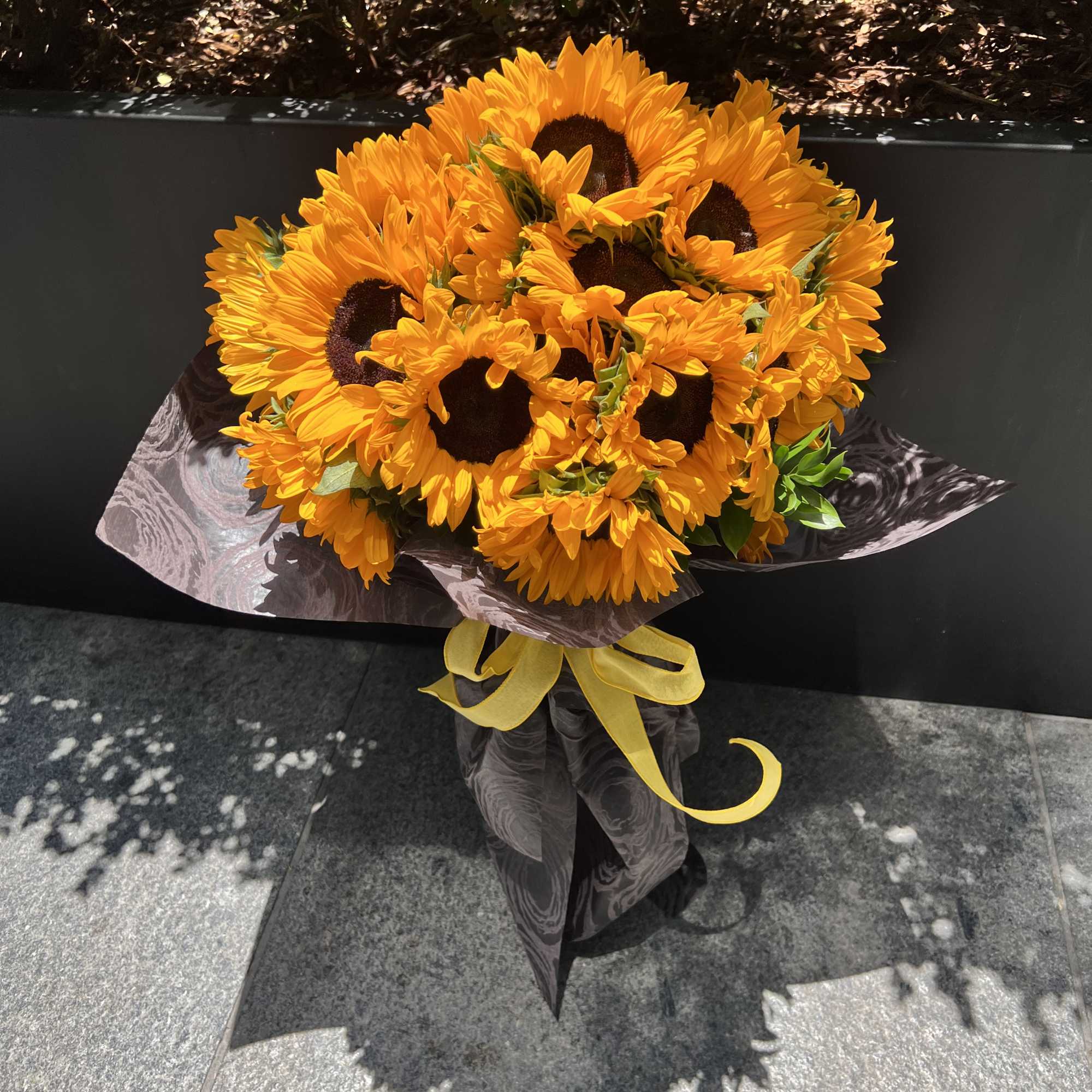 Bouquet of bright yellow sunflowers wrapped in dark paper with a yellow ribbon, photo 2 of 6