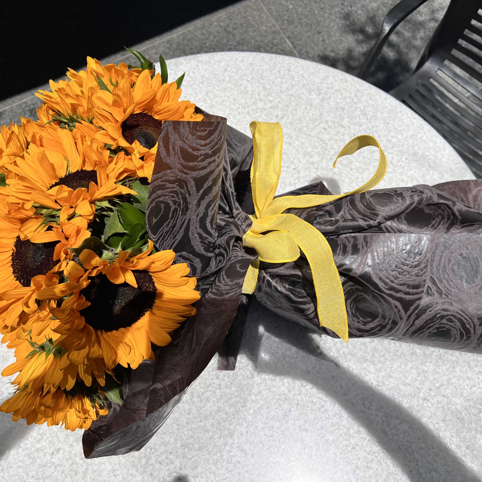 Bouquet of orange sunflowers wrapped in dark paper with a yellow ribbon