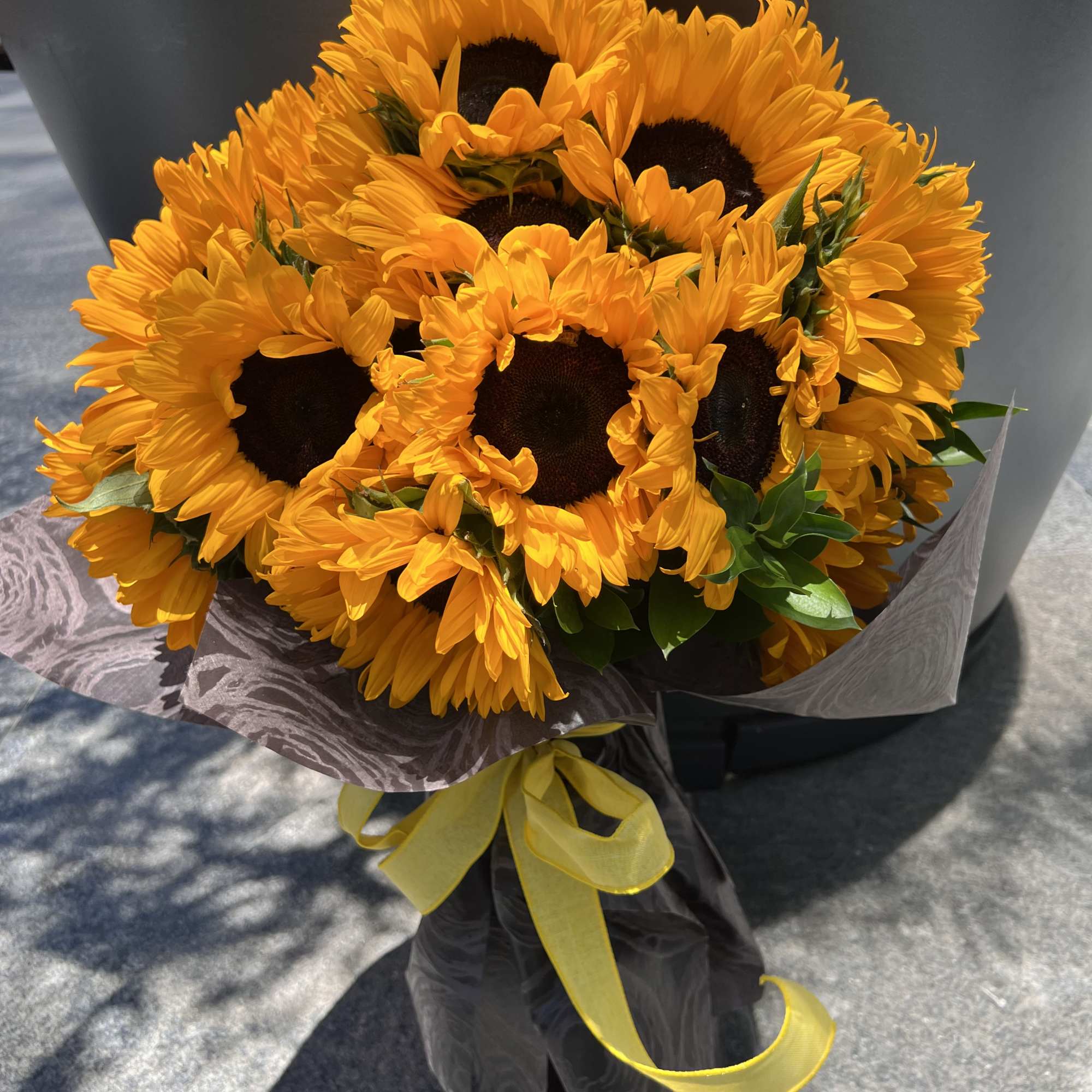 Bouquet of bright yellow sunflowers wrapped in dark paper with a yellow ribbon, photo 6 of 6