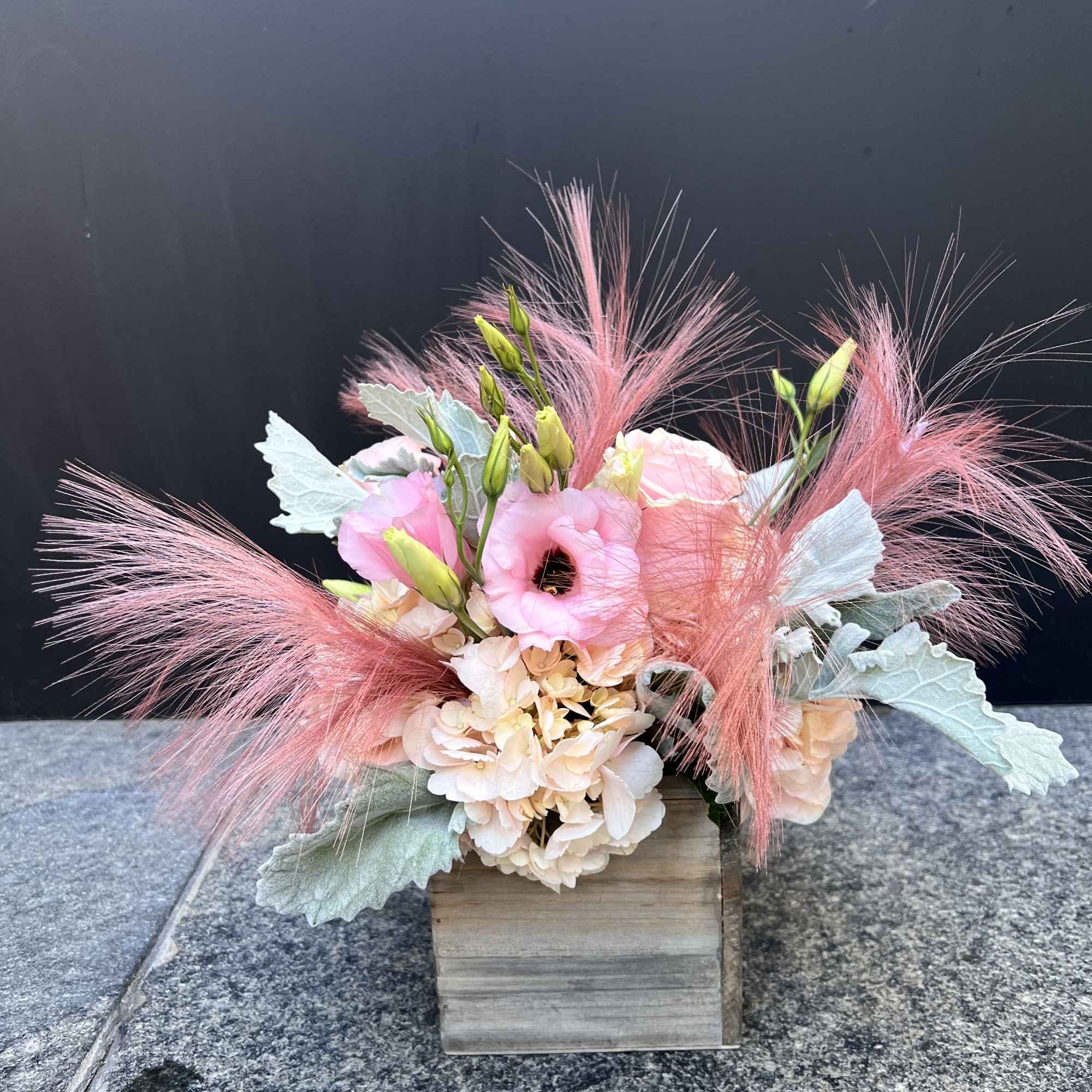 Pink and peach floral arrangement in a wooden box with feathery accents