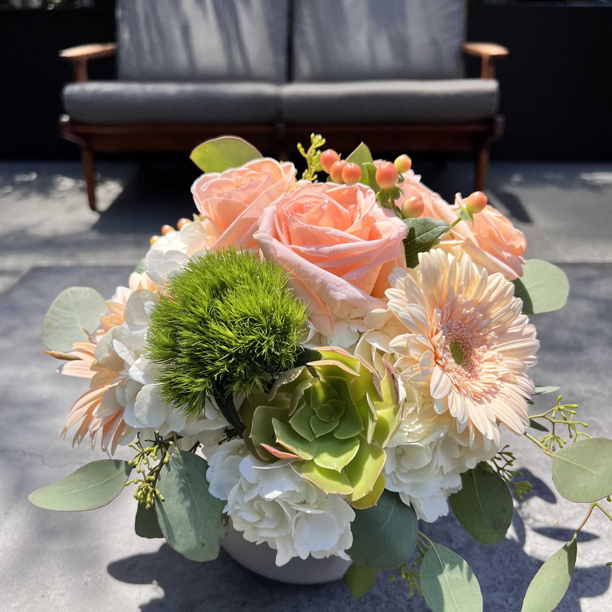Peach roses and pale daisies in a low vase with green succulent accents