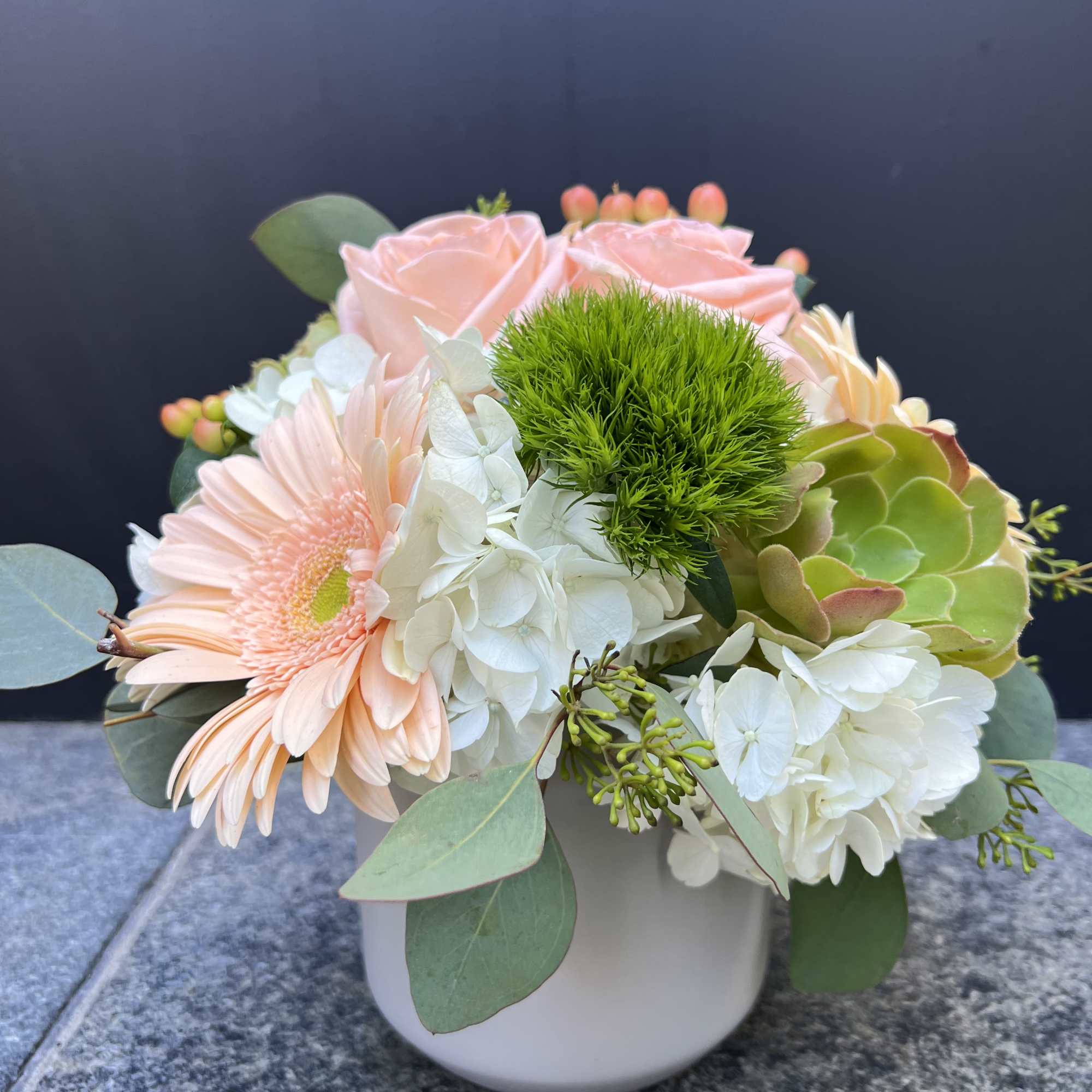 Peach roses and white hydrangeas in a white vase with green accents