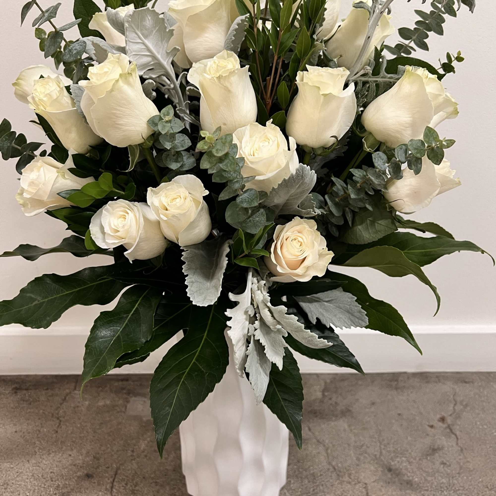 White roses arranged in a tall white vase with silver-green foliage