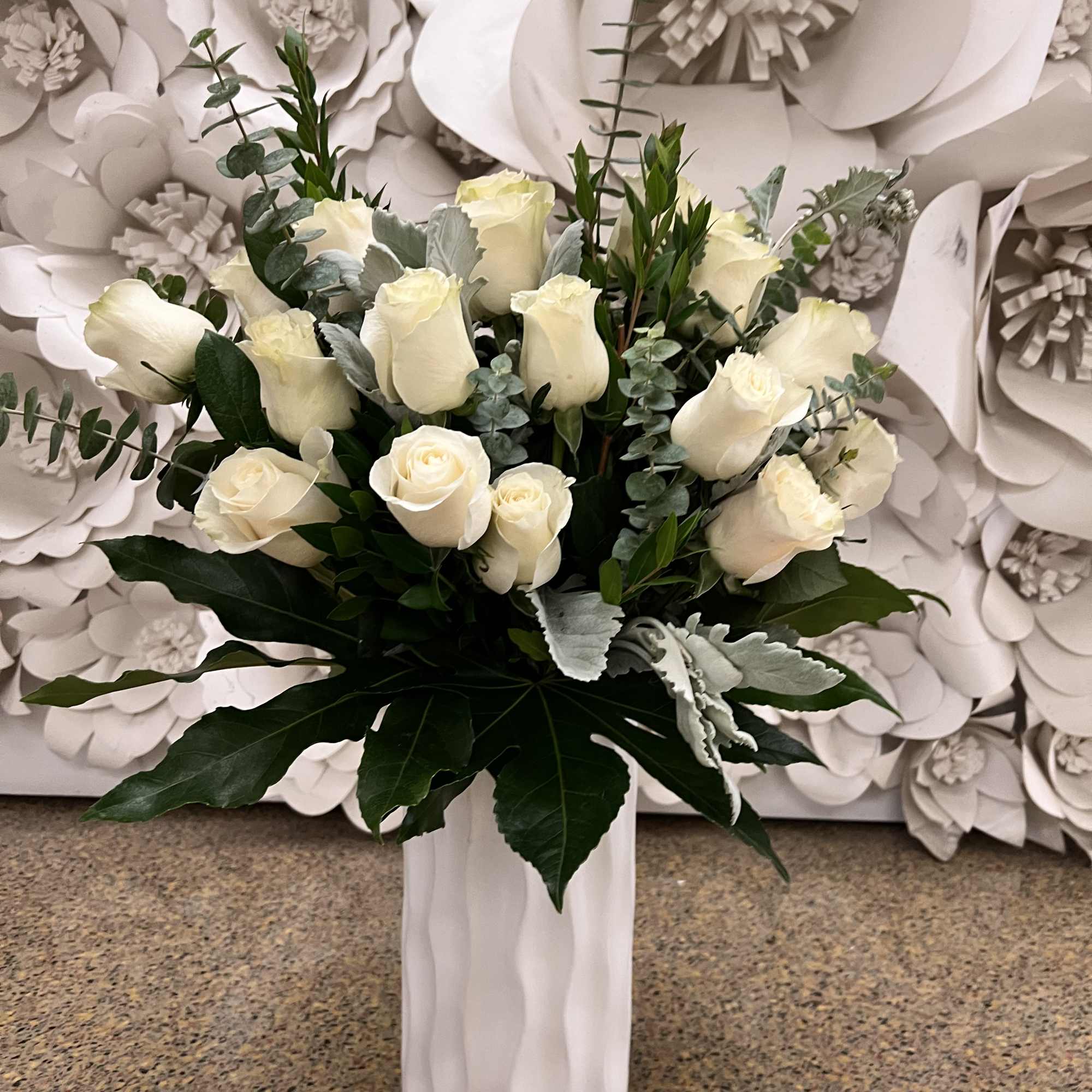 White rose bouquet in a tall white vase with greenery